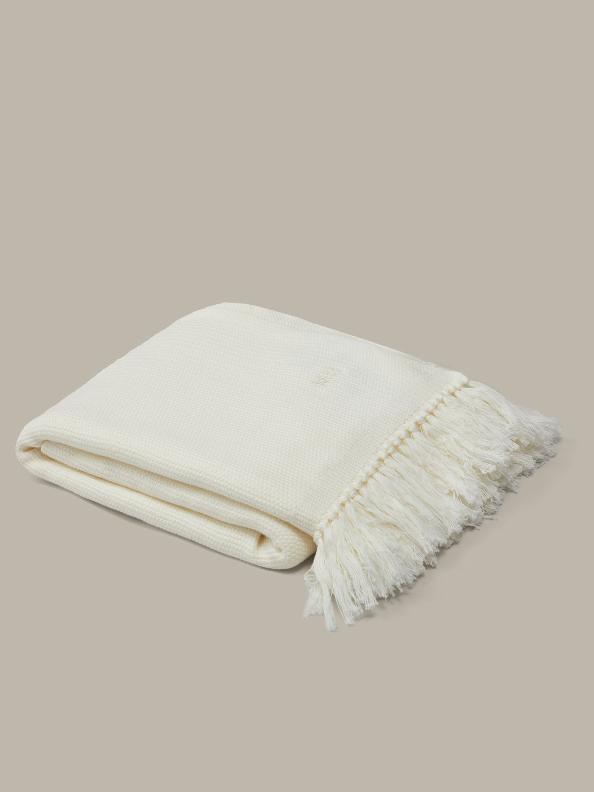 Folded cream-colored blanket with fringes on a beige background