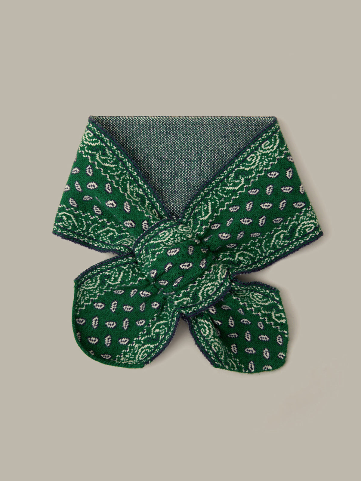 A folded green silk scarf with a white paisley bandana print and a solid dark green reverse side, displayed on a neutral beige background.