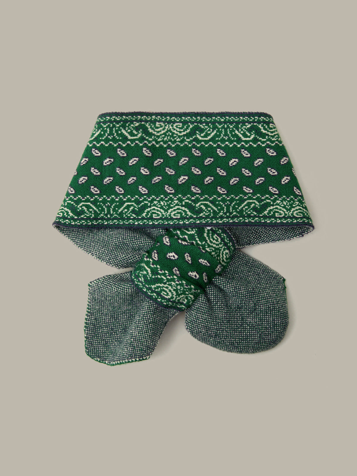 A green bandana-style neck gaiter with a paisley pattern, folded and tied in a bow, shown on a solid beige background.