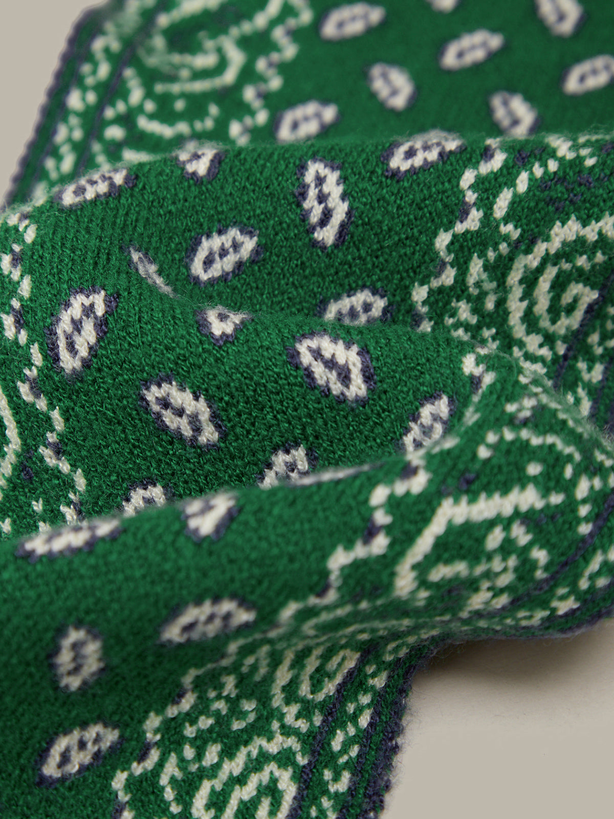 A close-up of a green knit fabric with a white and purple paisley pattern, draped in soft folds against a light neutral background.