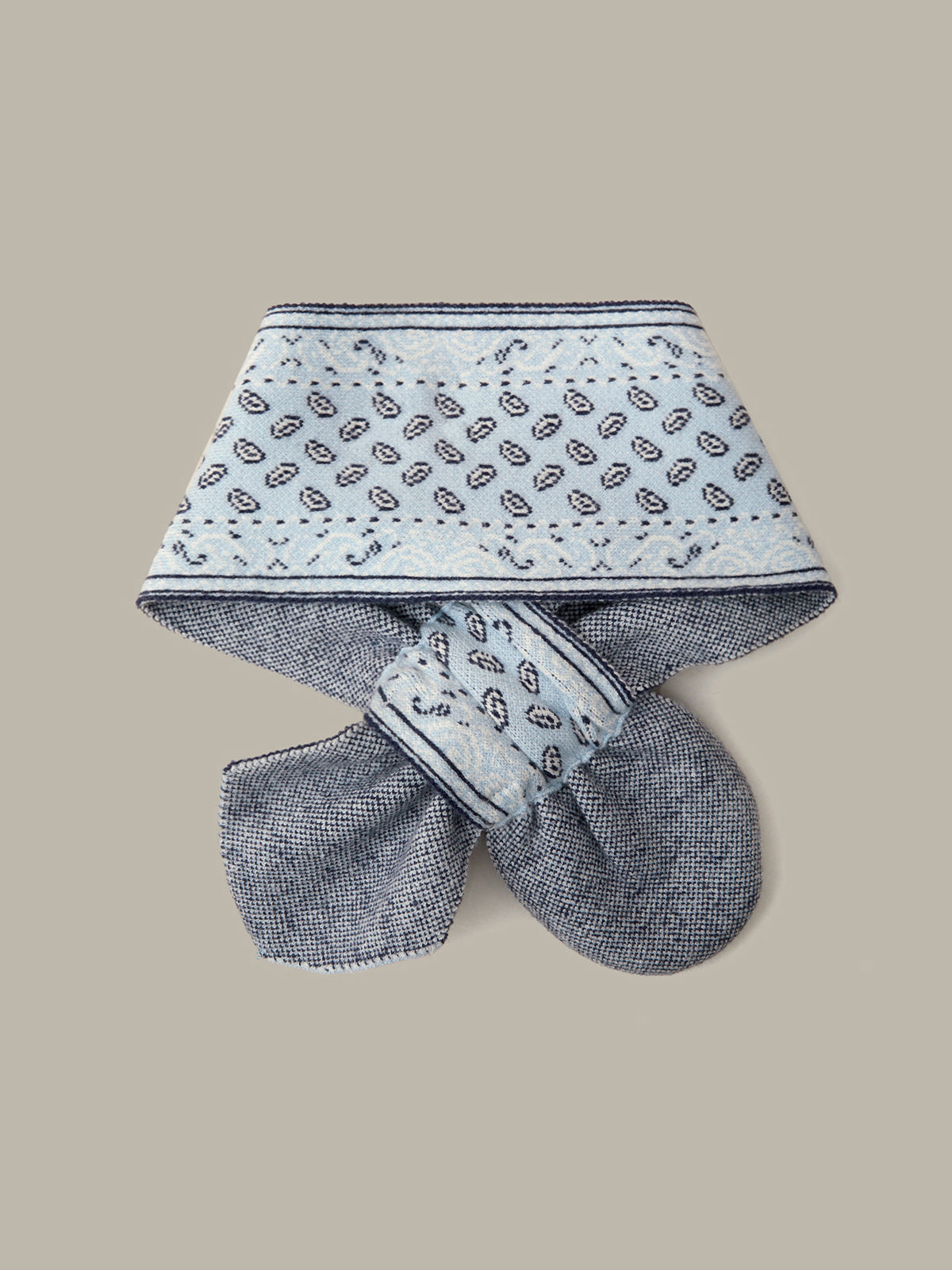 A baby bootie or soft bootie with a matching fabric head covering, featuring a white top section with a black paisley pattern and a textured gray-blue bottom section, displayed on a solid beige background.