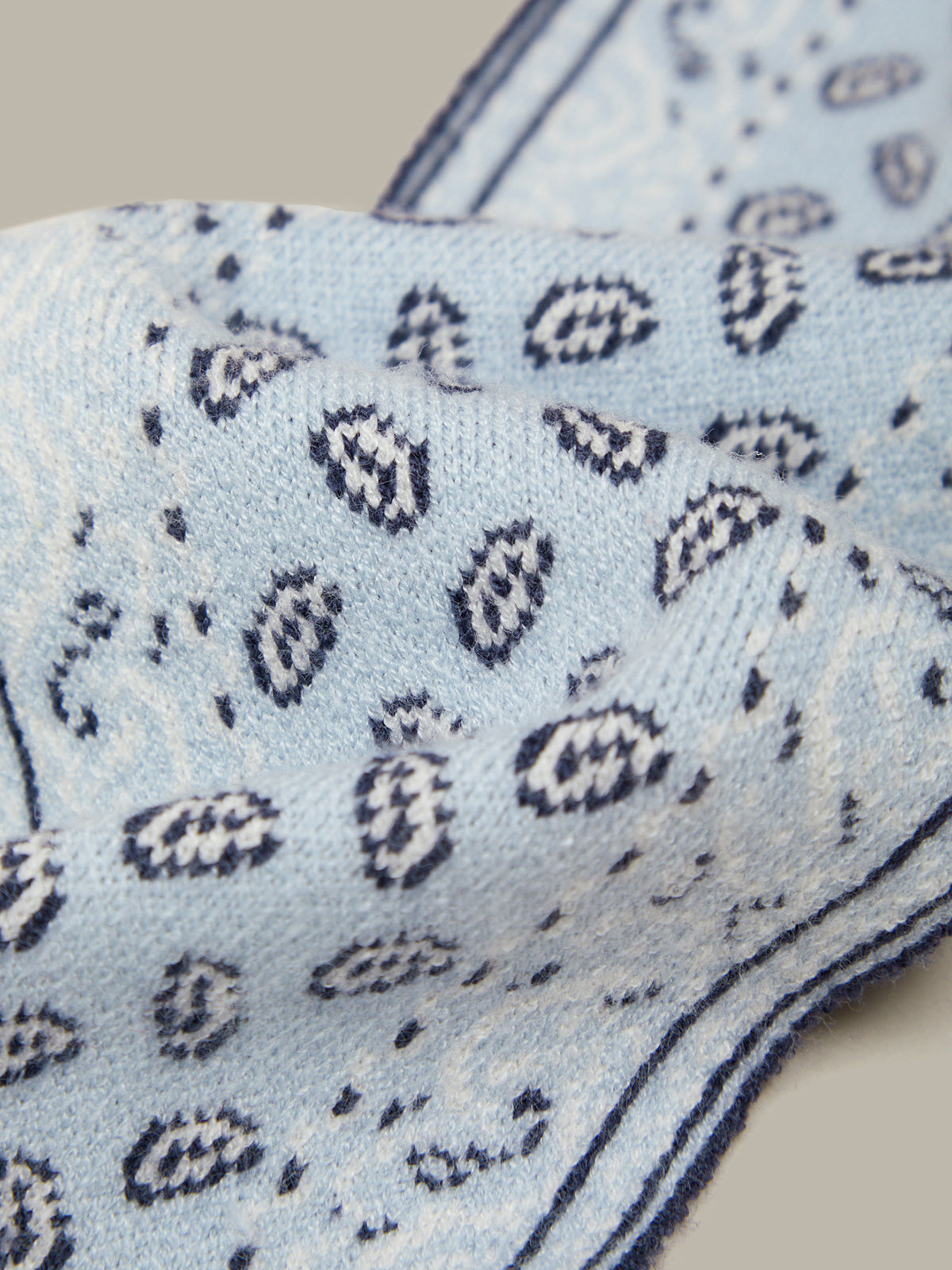 A close-up of a light blue knit fabric with a navy blue paisley pattern and a matching border.