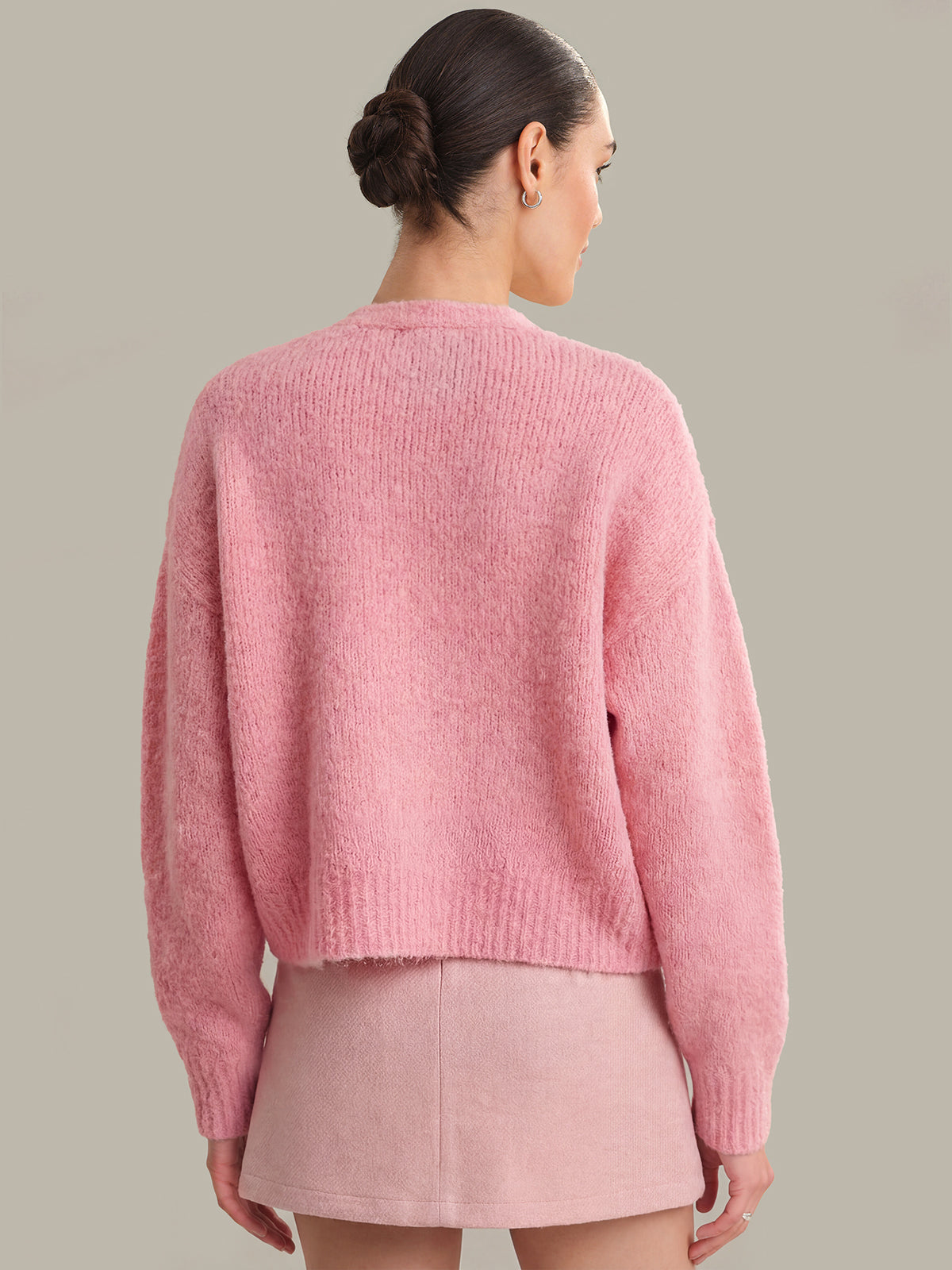 Person wearing a pink sweater and skirt set against a neutral background
