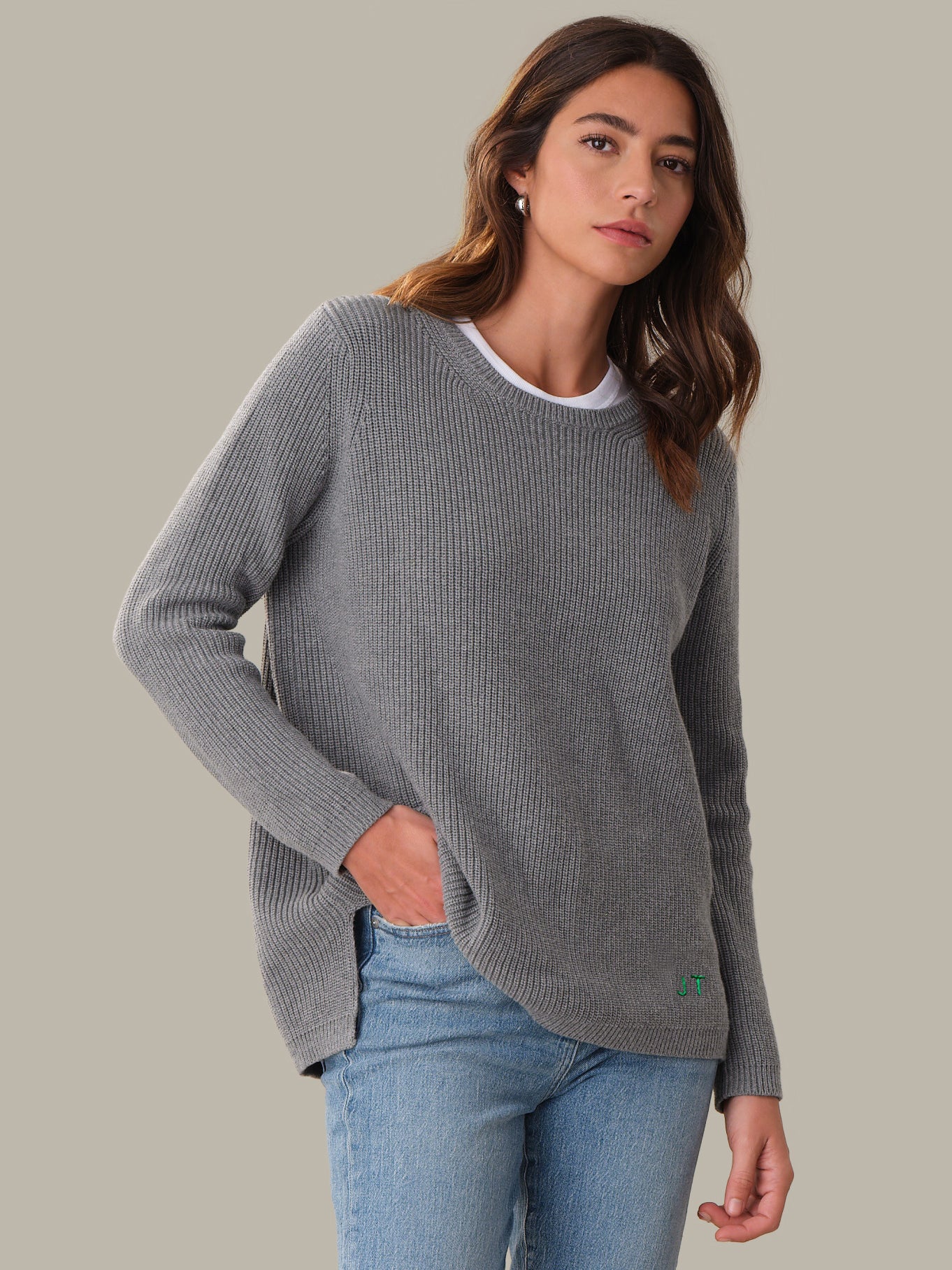 Woman wearing a gray sweater and blue jeans against a plain background