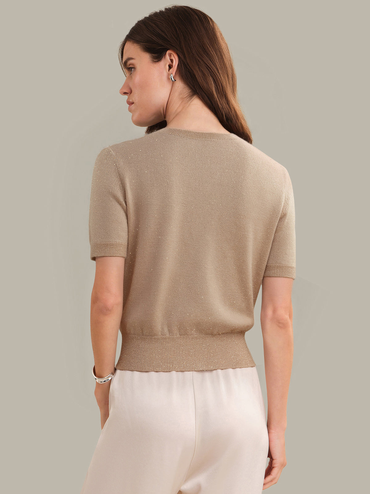 Woman wearing a beige sweater and white pants against a neutral background