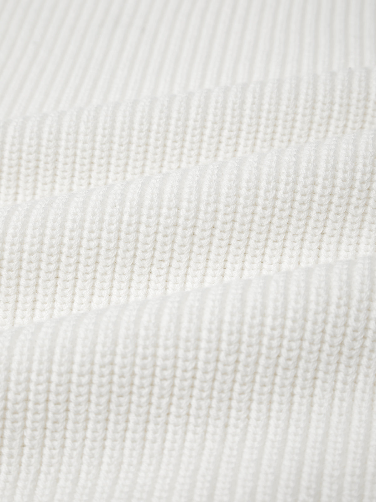 Close-up of a white, ribbed knit fabric that mirrors the texture of a 525 America cotton shaker stitch sweater. The parallel ribbing creates uniform rows, indicating a soft, stretchy material ideal for crafting pieces with a fitted silhouette.