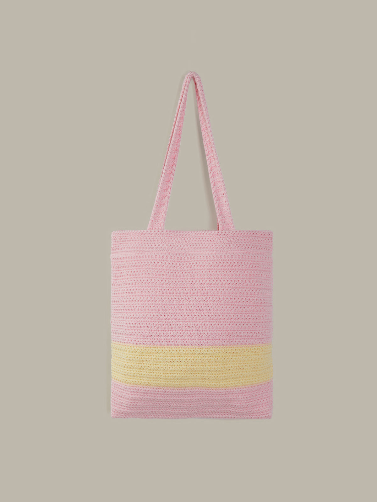 A pink woven tote bag with a wide horizontal yellow stripe near the bottom and matching pink shoulder straps, shown against a solid taupe-gray background.