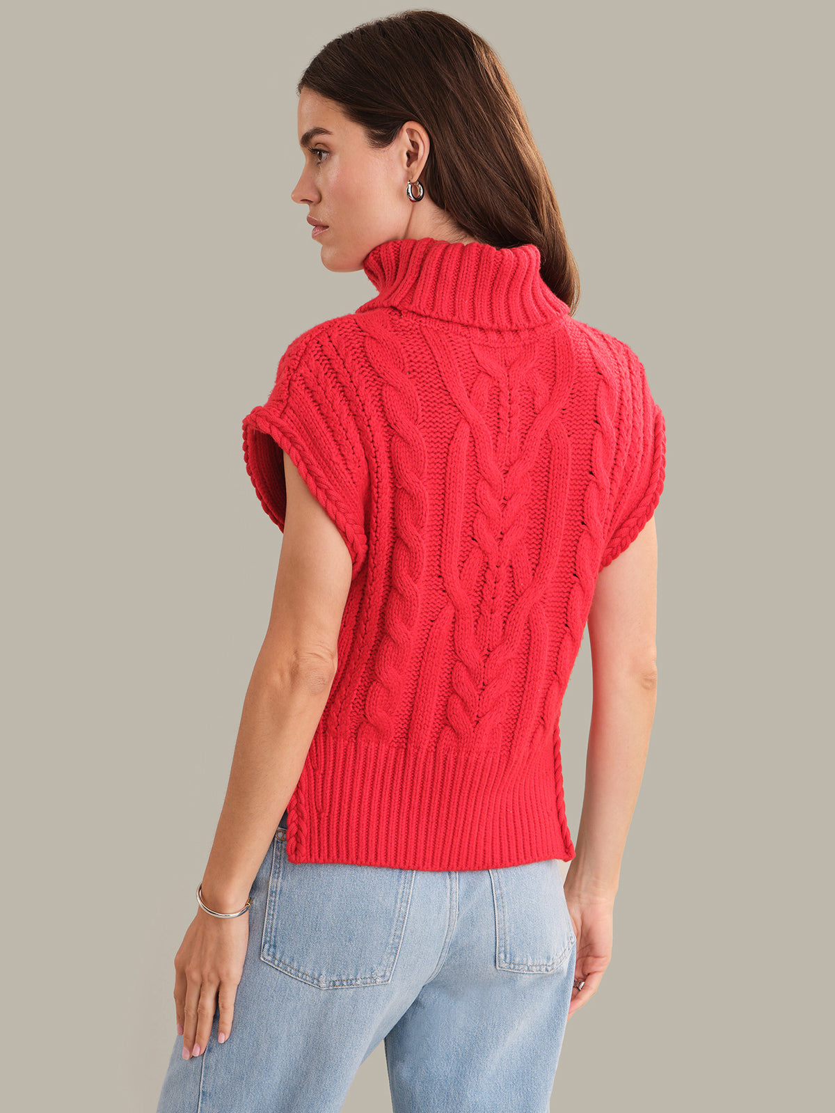 Woman wearing a red knitted sleeveless sweater against a plain background