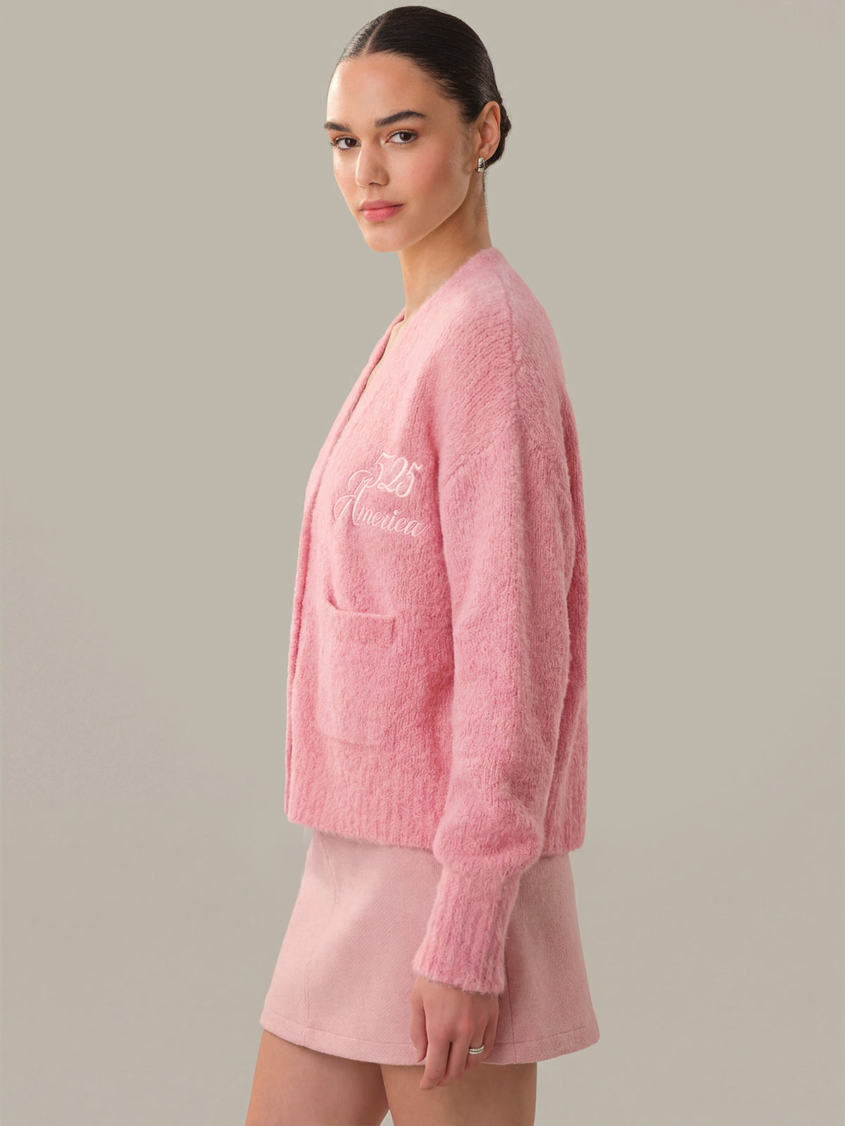 Woman wearing a pink textured cardigan and skirt set against a neutral background