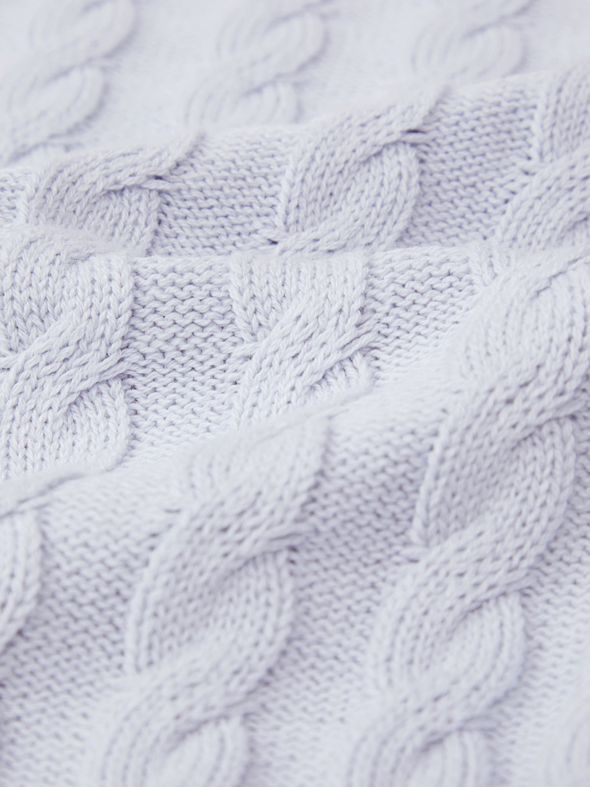 Close-up of a soft, light gray cable knit fabric by 525 America, showcasing a classic pattern. The texture features intertwining loops typical of cable stitches, creating a raised design that suggests a relaxed silhouette.
