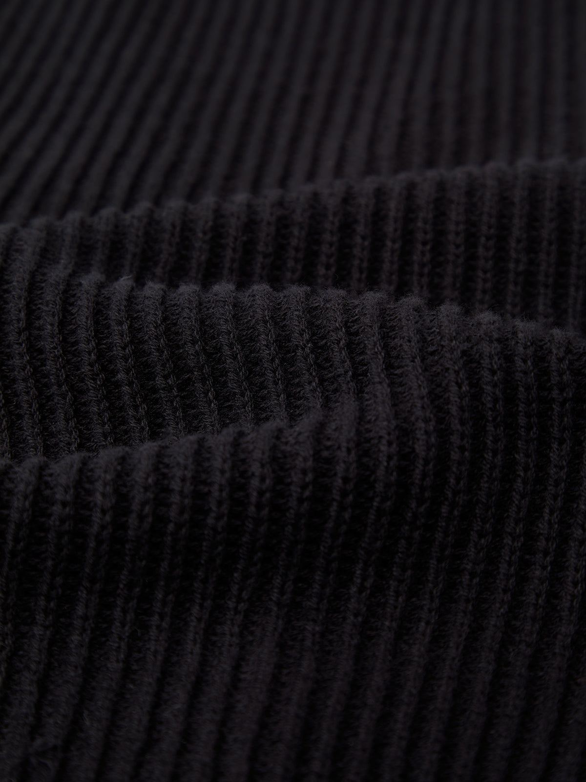 Close-up of 525 Americas black ribbed fabric, resembling a chic cable knit cardigan with soft, evenly spaced vertical lines and knitted texture forming parallel ridges.