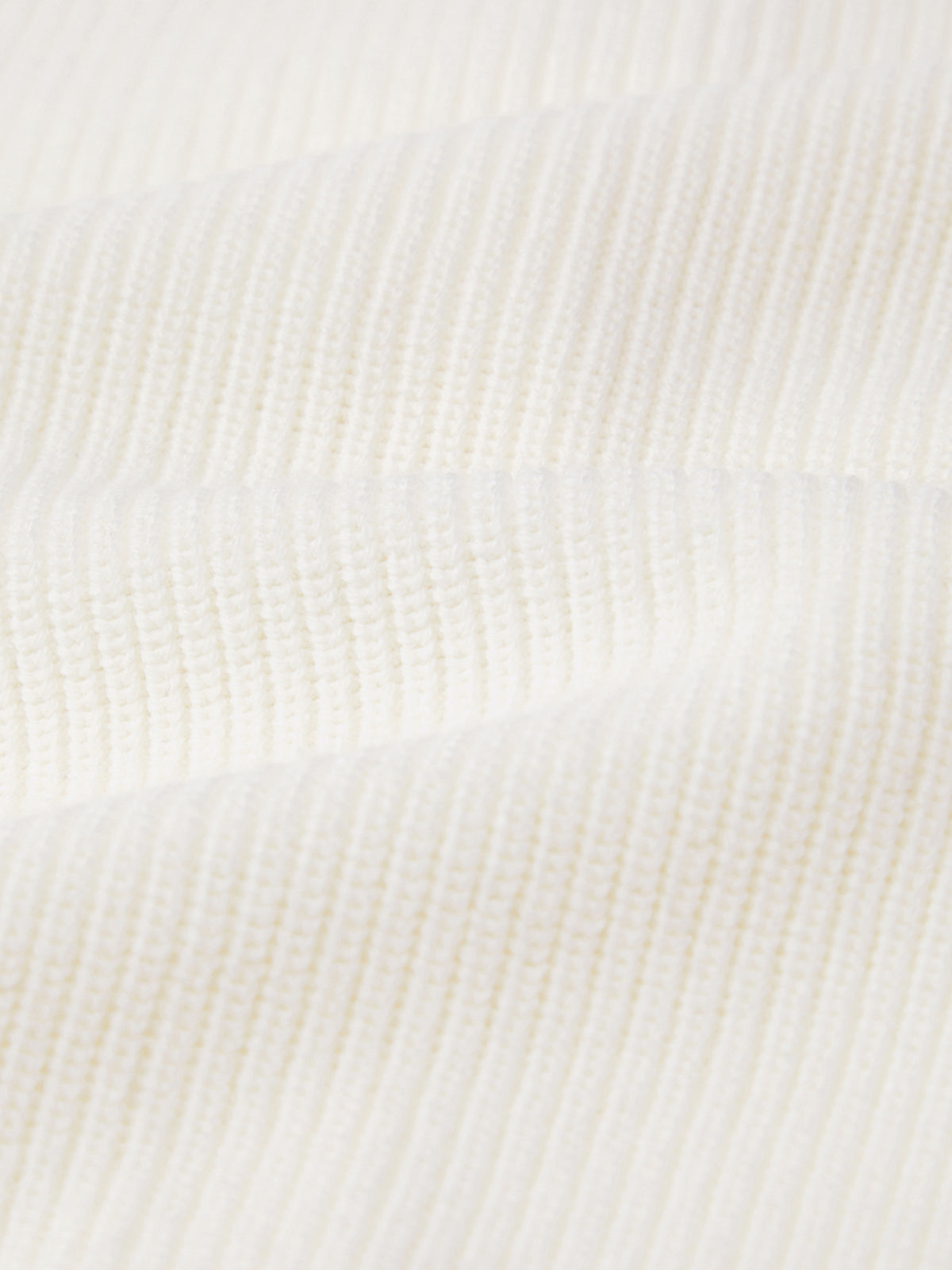 A close-up of 525 Americas white ribbed fabric showcases a textured pattern, reminiscent of soft cotton. The horizontal ridges suggest softness and elasticity, while the gentle wave formation highlights its texture and weave in a relaxed silhouette.
