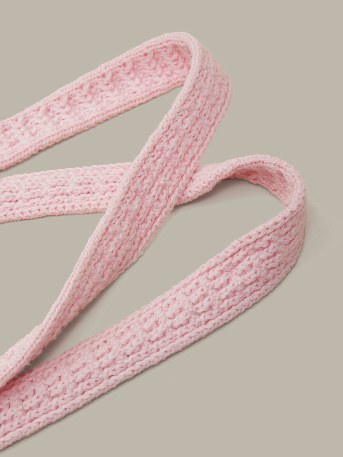 A close-up of a light pink textured crochet strap, likely a camera strap or belt, arranged in loops against a solid neutral gray background.