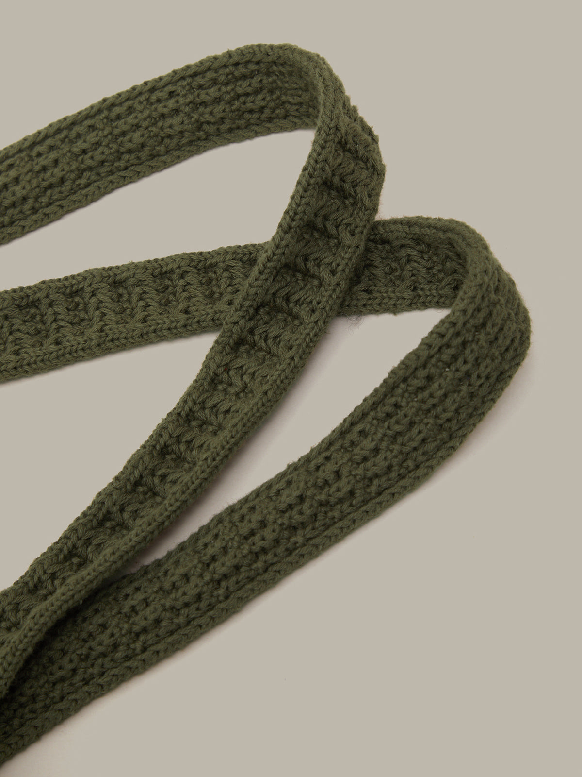 An olive green knitted strap with a textured cable pattern, draped in a loop against a solid light gray background.