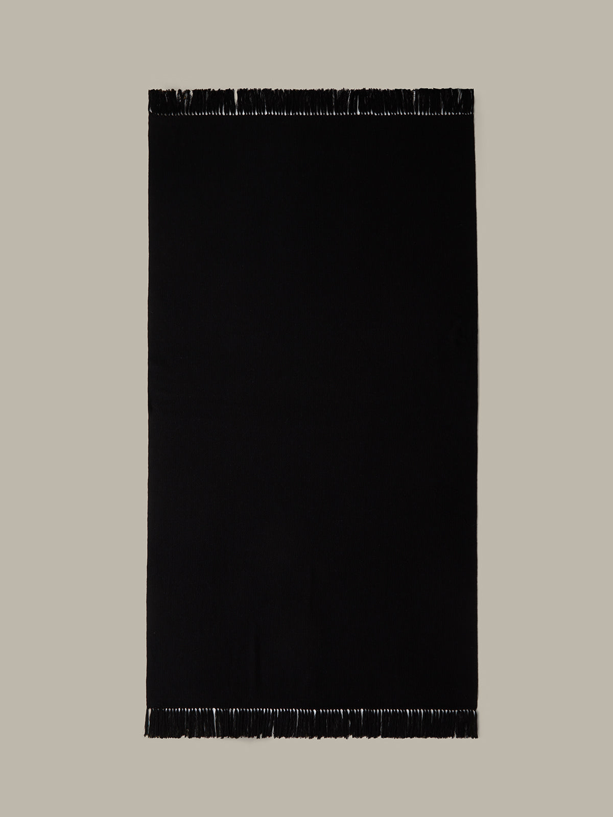 Black rectangular rug with fringe on a beige background