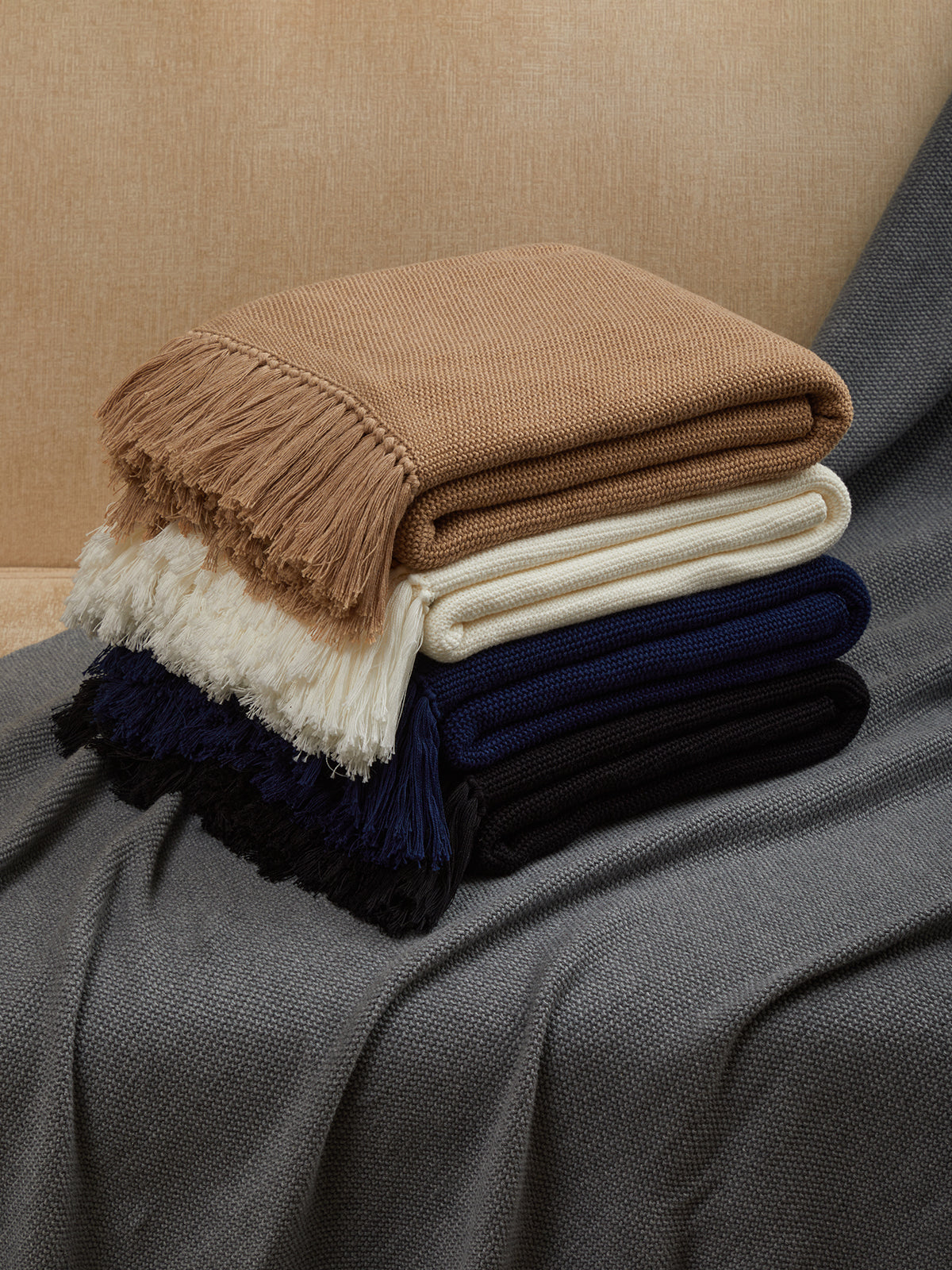 Stack of folded blankets in brown, white, and navy on a textured surface.