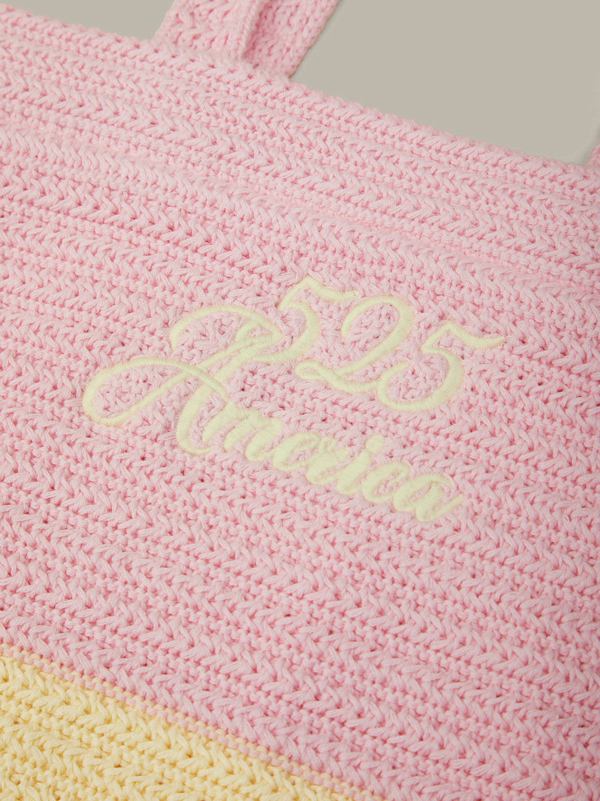 Close-up of a pink woven tote bag with pale yellow embroidered script reading '525 America' and a matching pale yellow woven band near the bottom.