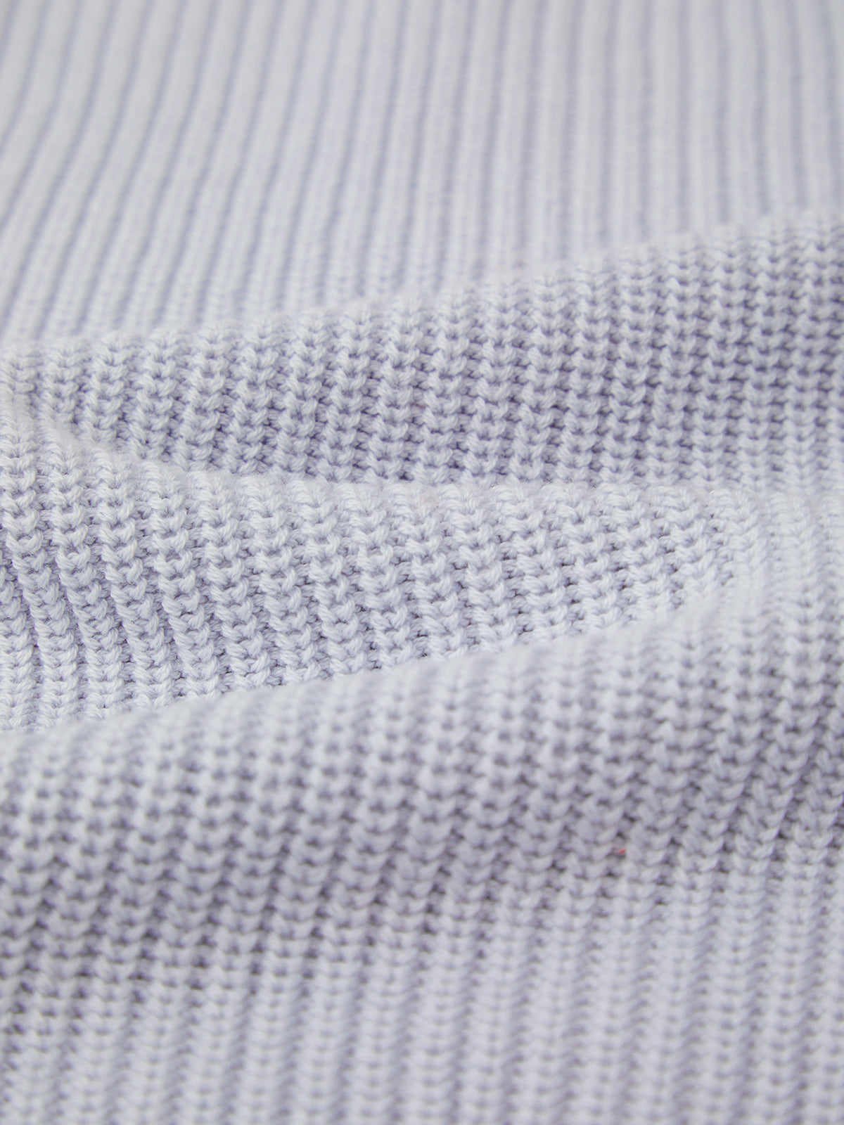 Close-up of 525 America’s white knitted fabric in a versatile shaker stitch, featuring horizontal ridges and detailed yarn work. Crafted from 100% cotton, this relaxed fit offers comfort and timeless texture.