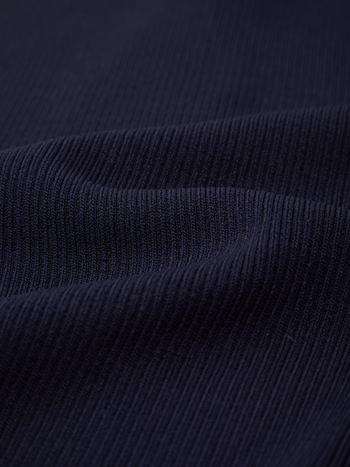 Close-up of 525 America’s dark navy blue ribbed fabric with soft folds, showcasing its fine vertical lines and texture—ideal for creating versatile pieces perfect for warm weather fashion.