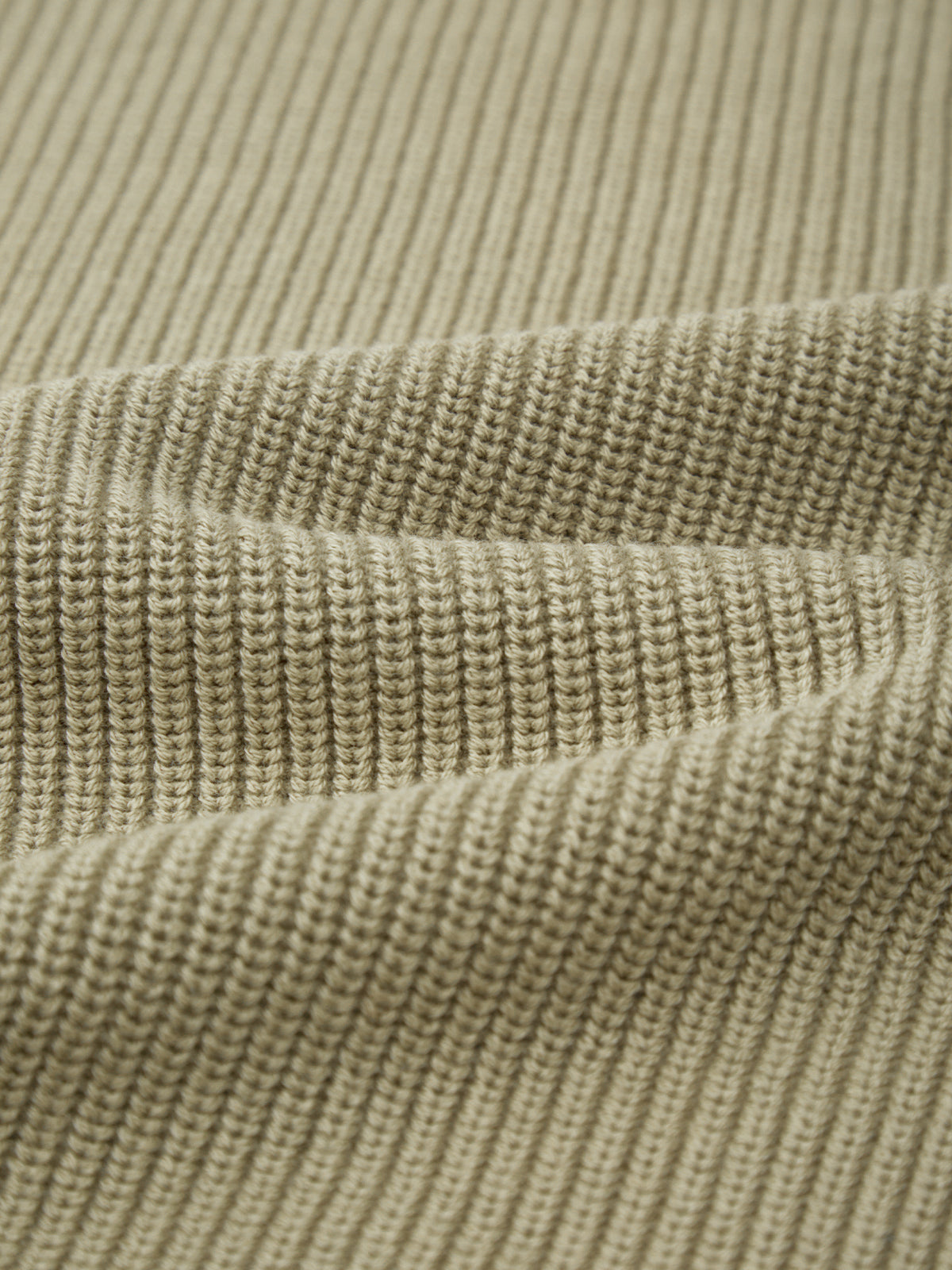 A close-up of 525 America’s beige ribbed knit fabric showcases a versatile shaker stitch pattern with distinct vertical lines and subtle folds.