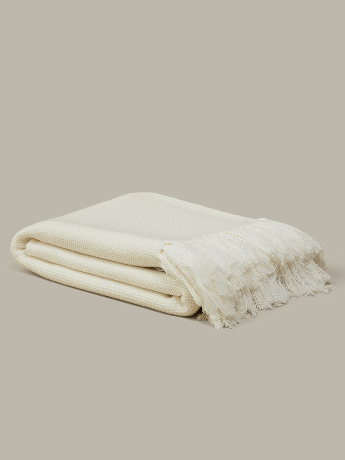 Folded cream-colored blanket with fringes on a beige background