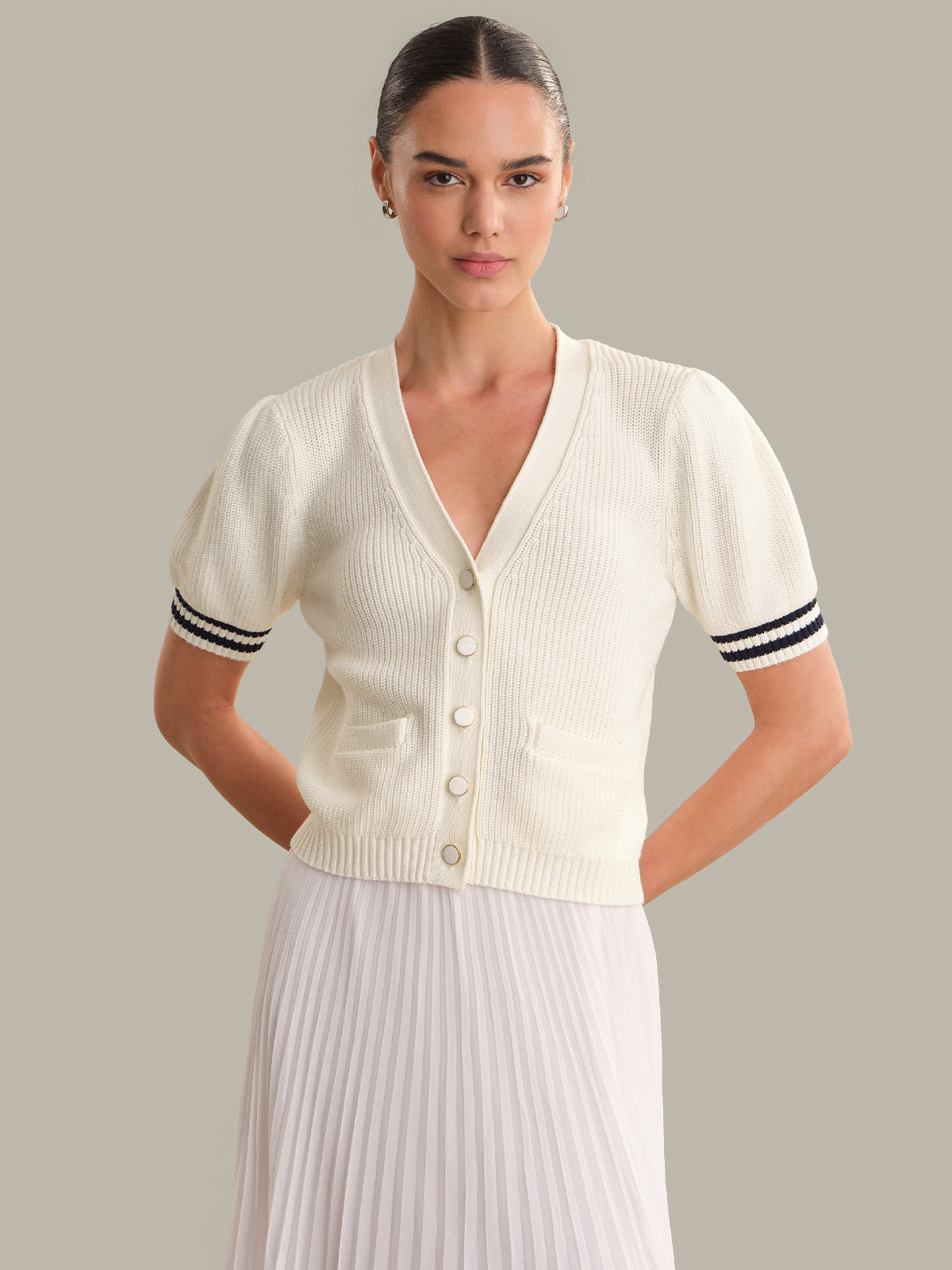 Woman wearing a white cardigan with black trim on a gray background