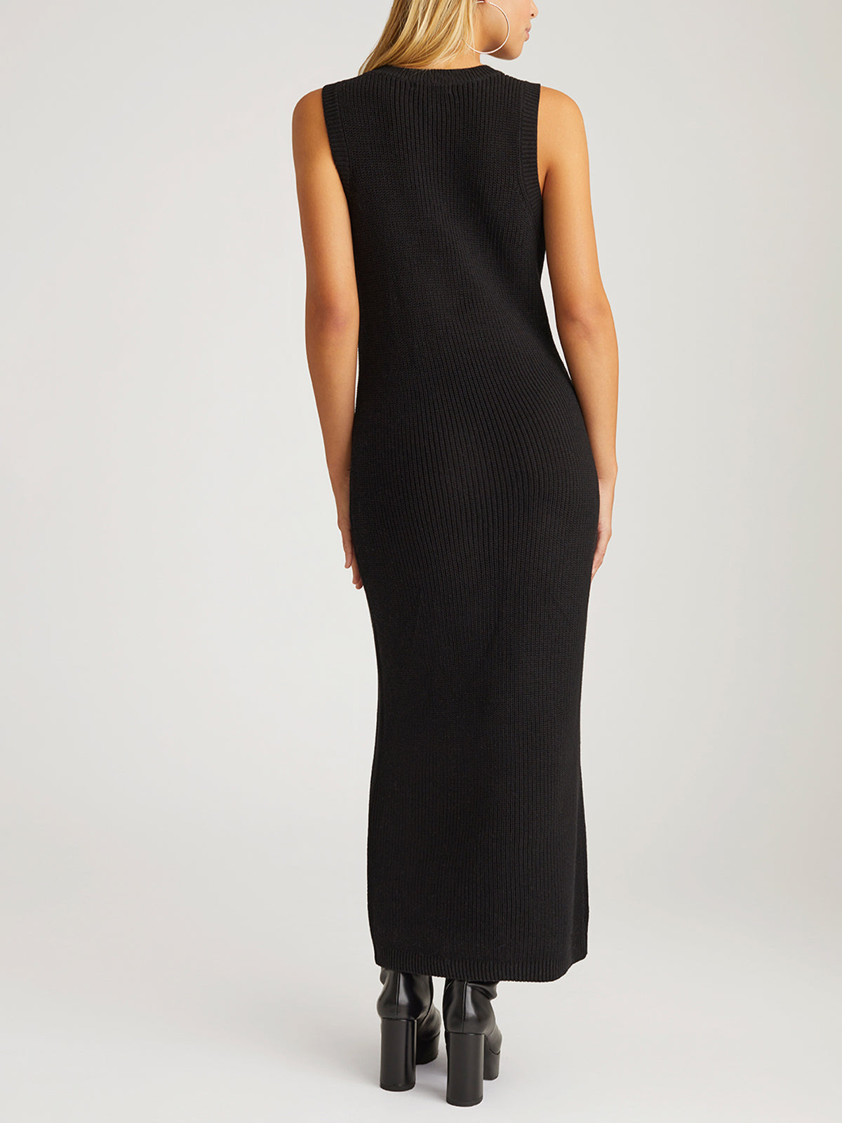A woman faces away, wearing a stylish and comfortable sleeveless, ankle-length black ribbed dress by 525 America. The outfit is paired with black platform boots and complemented by her long blonde hair against a simple light gray background.