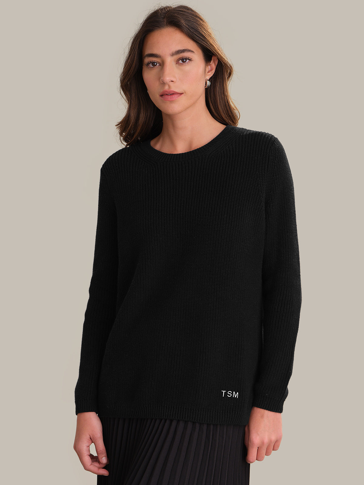 Woman wearing a black sweater with 'TSM' logo on a beige background