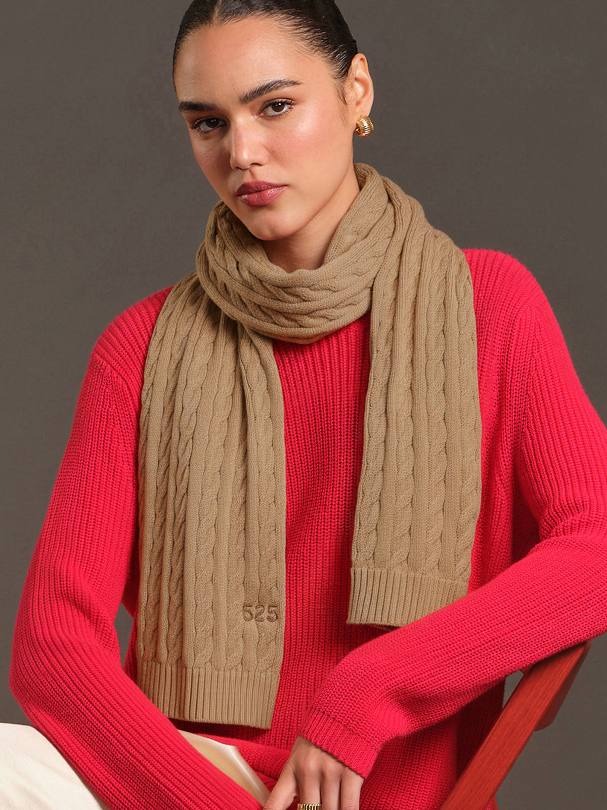 Woman wearing a red sweater and beige scarf against a gray background
