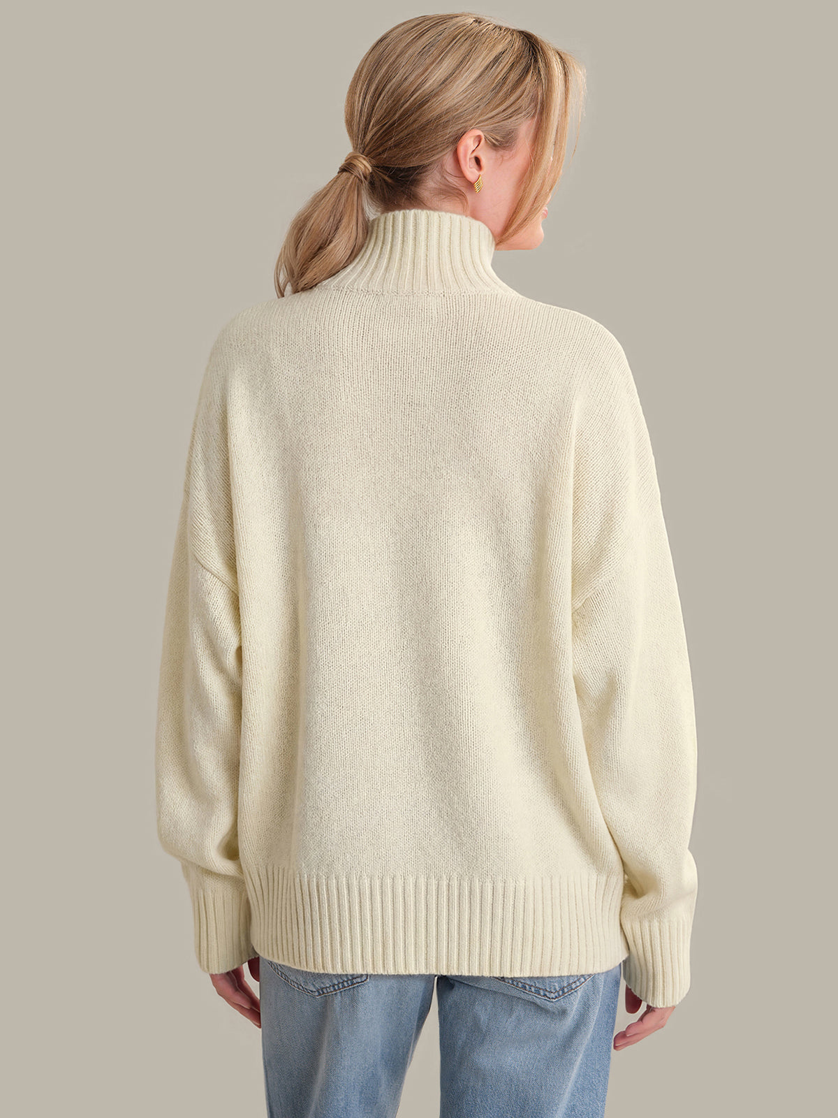 Person wearing a cream sweater and blue jeans against a plain background