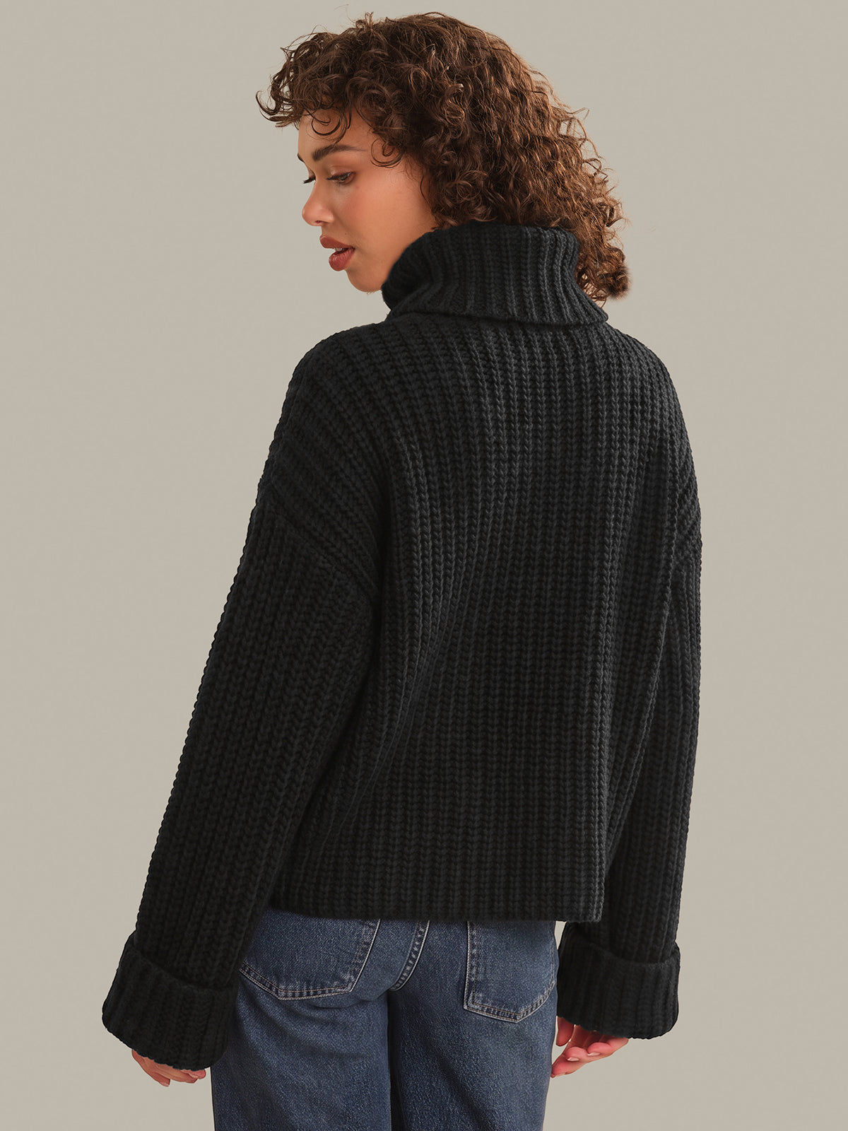 Person wearing a black ribbed sweater and blue jeans on a plain background
