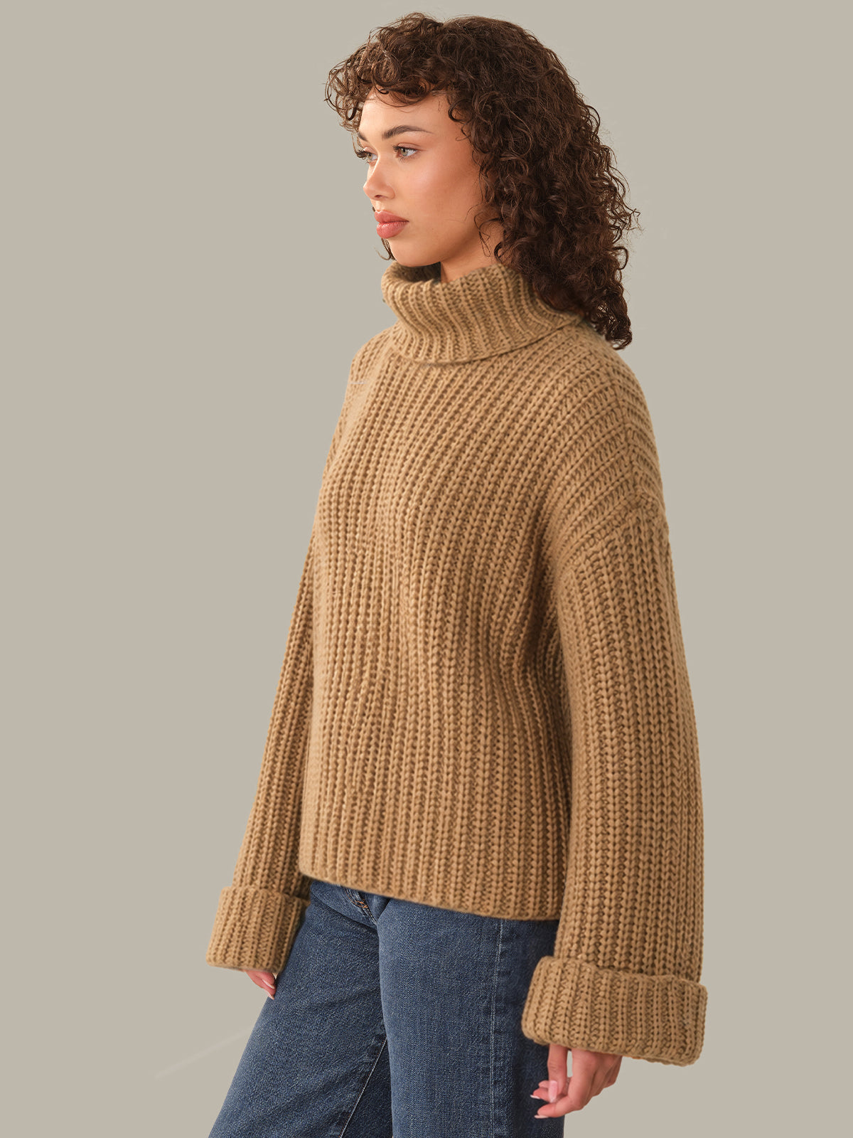 Woman wearing a brown knitted sweater and blue jeans on a gray background