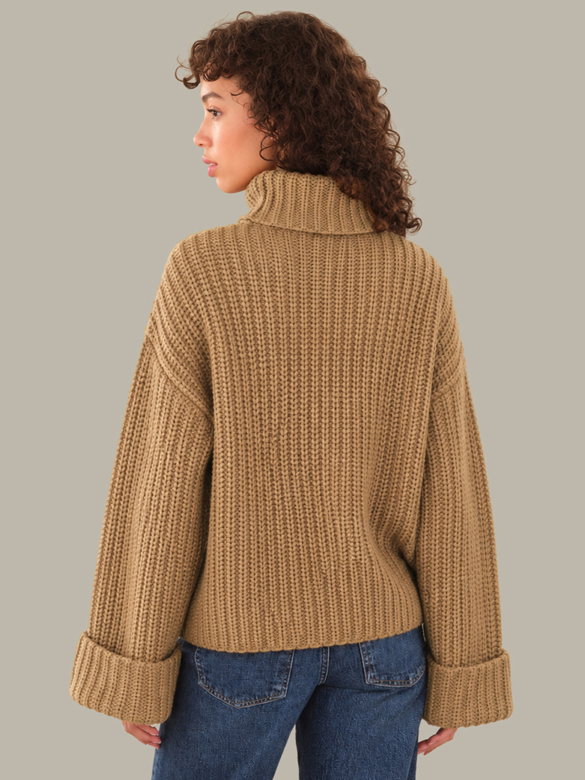 Woman wearing a beige knitted sweater and blue jeans on a gray background