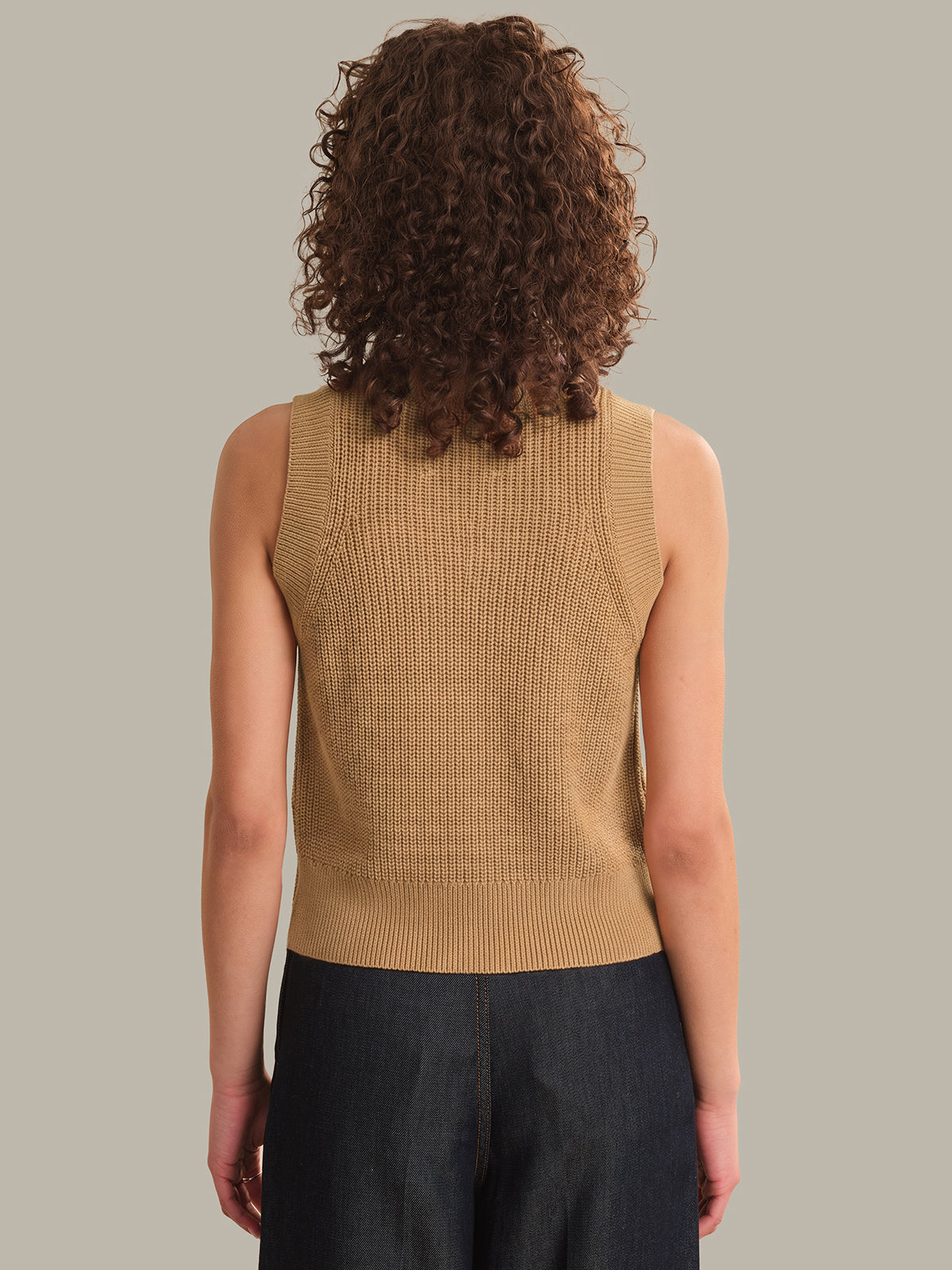 Person wearing a beige sleeveless knitted top against a neutral background