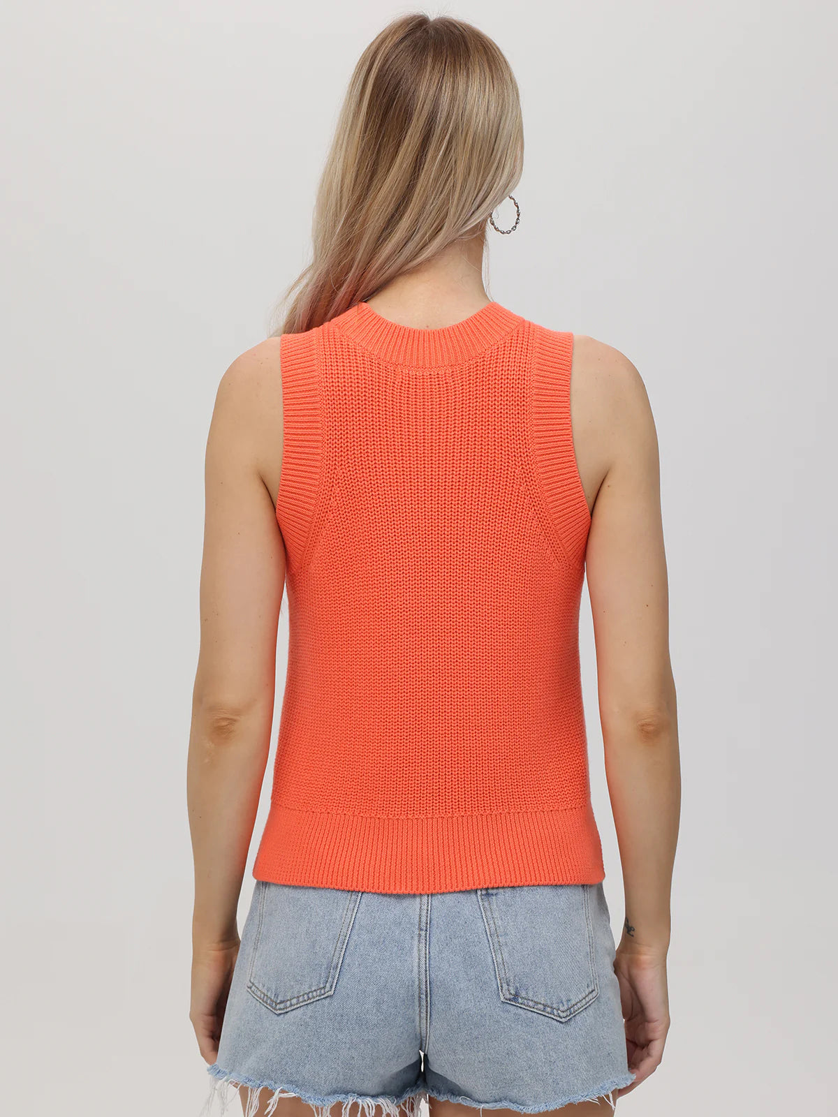 Person wearing an orange sleeveless sweater against a plain background