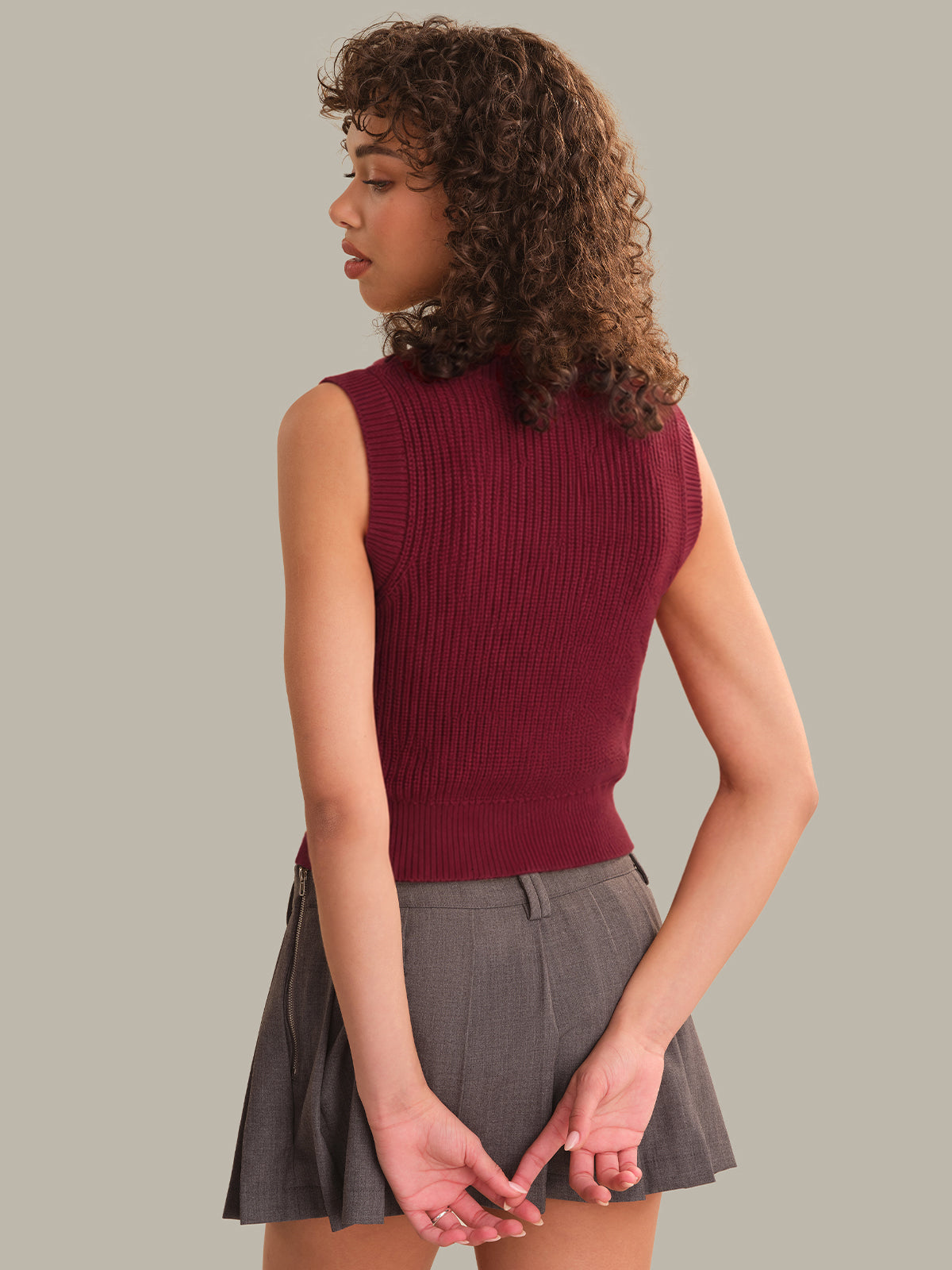 Woman wearing a maroon sleeveless top and gray skirt on a plain background