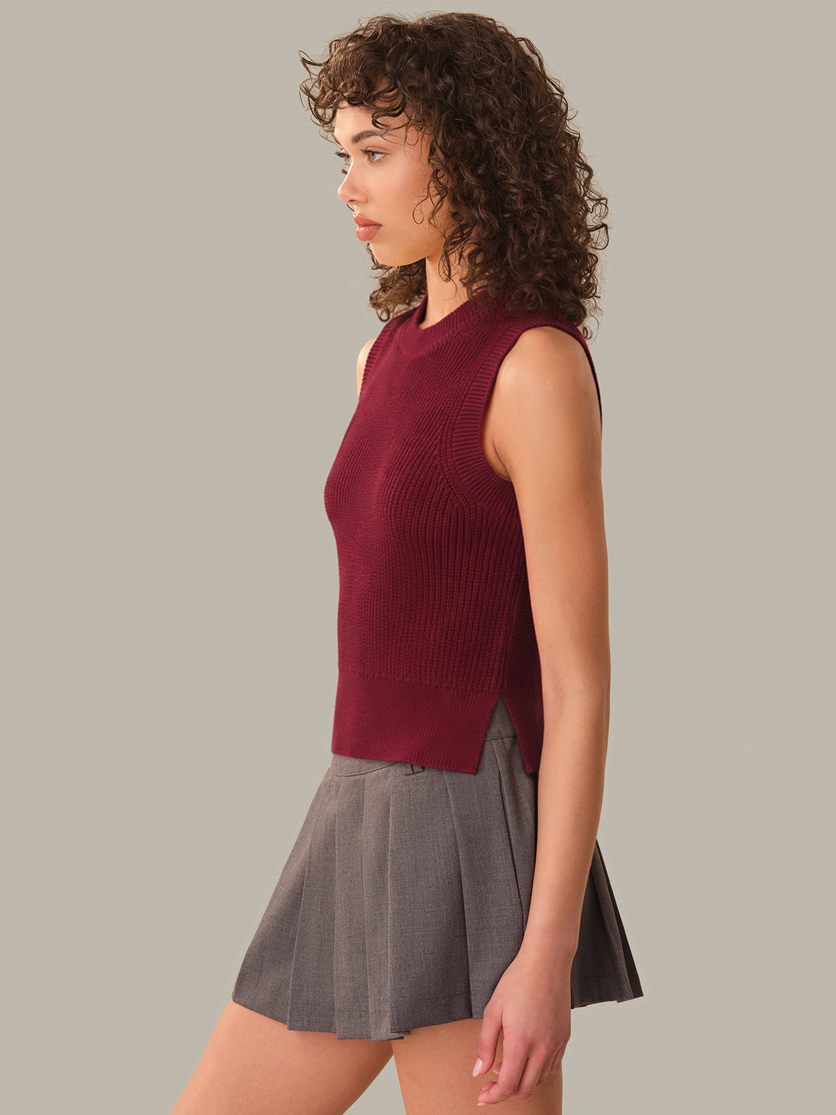 Woman wearing a maroon sleeveless top and gray skirt on a plain background