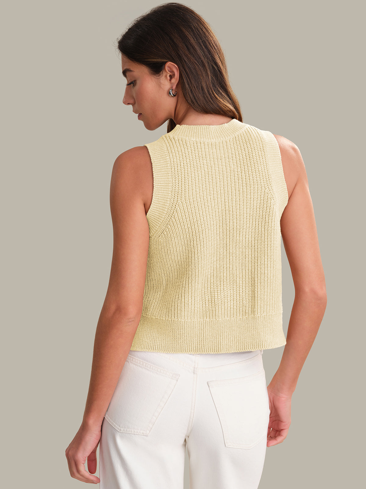 Woman wearing a light yellow sleeveless knitted top against a neutral background