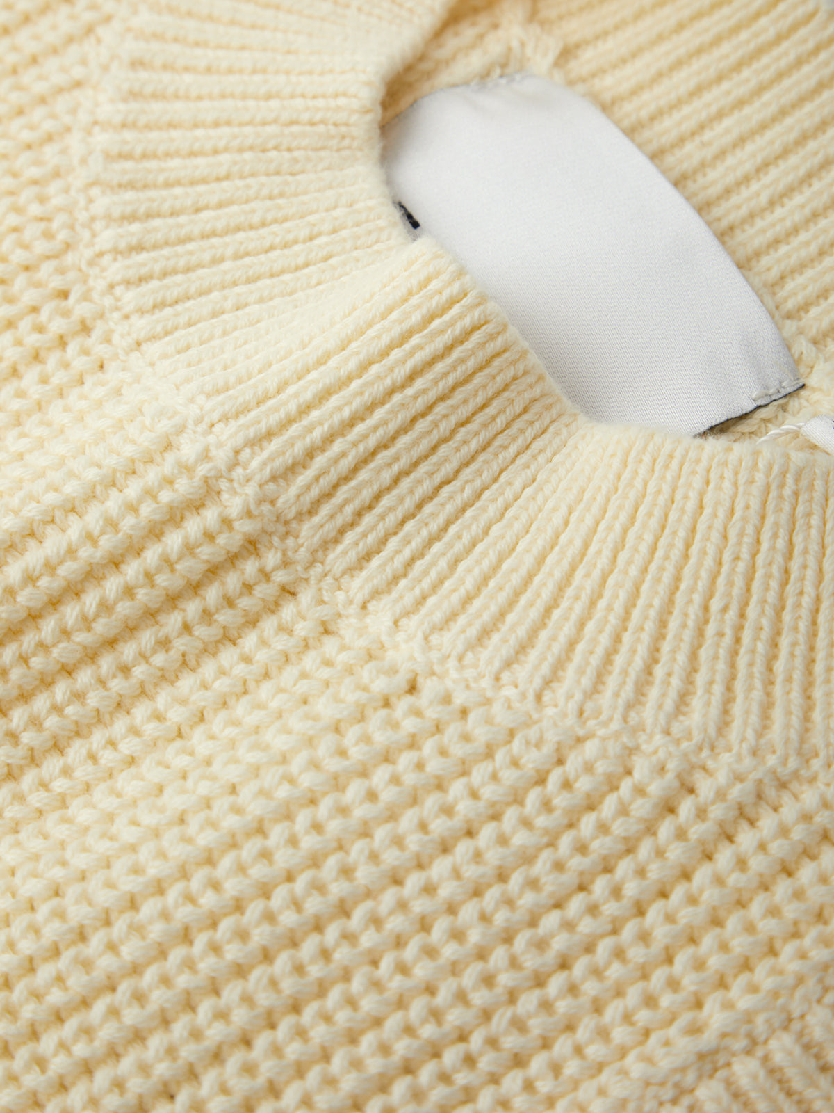 Close-up of a beige knitted sweater with a white tag.
