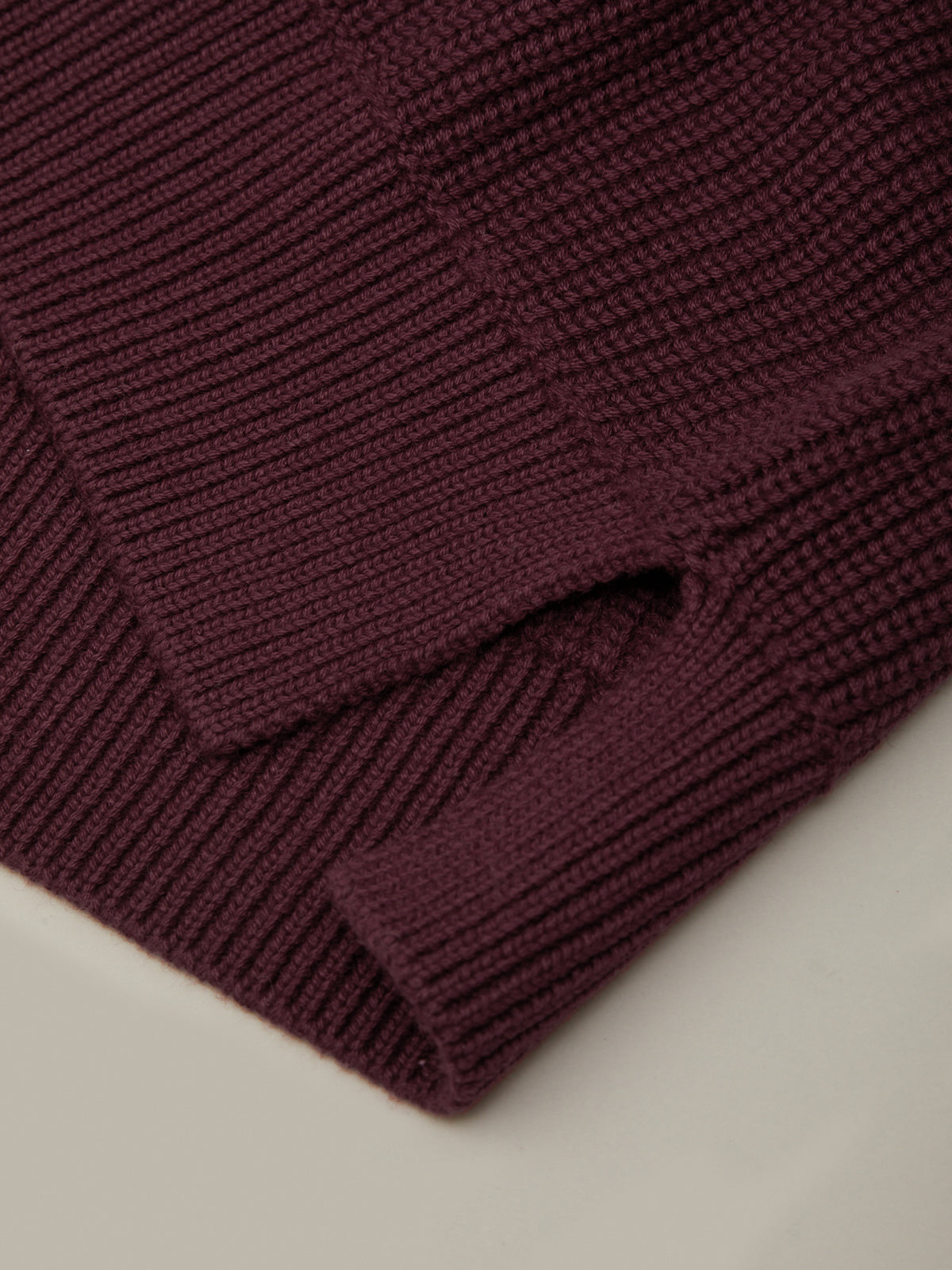Close-up of a burgundy knitted sweater on a light beige background