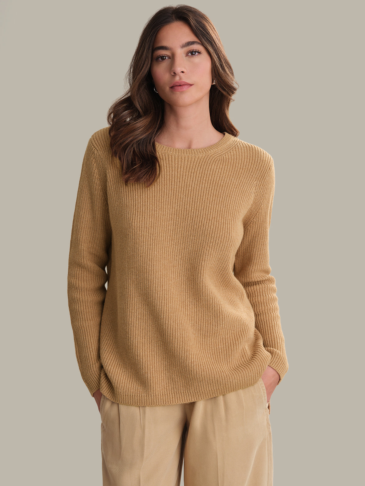 Woman wearing a beige sweater and pants against a neutral background