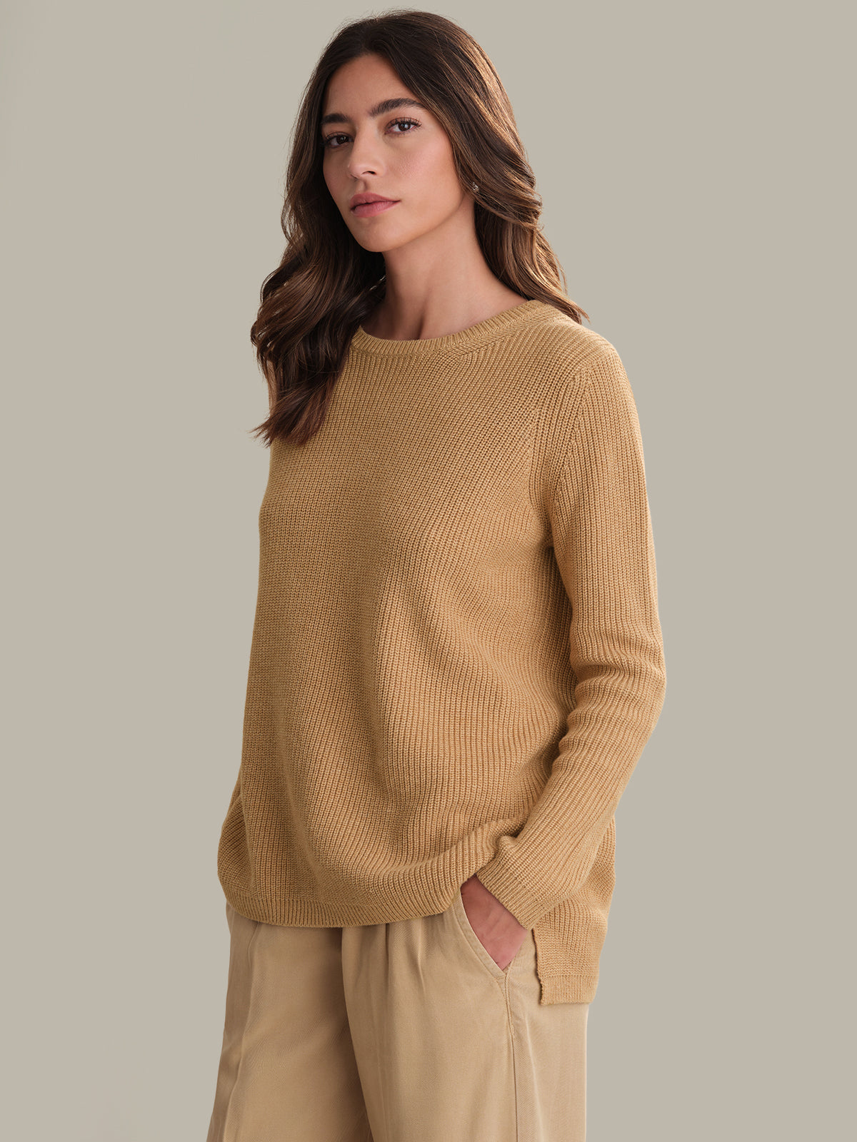 Woman wearing a mustard yellow sweater and pants against a neutral background