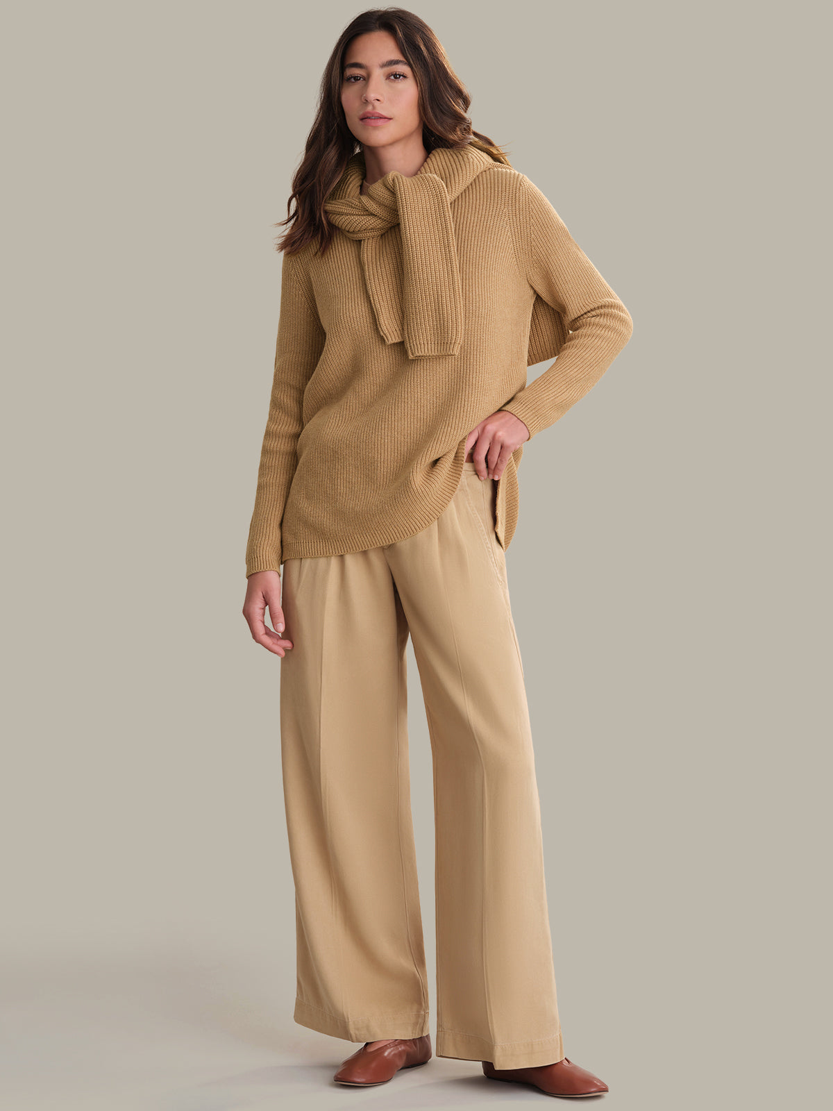 Woman wearing a beige sweater and pants with a matching scarf on a neutral background