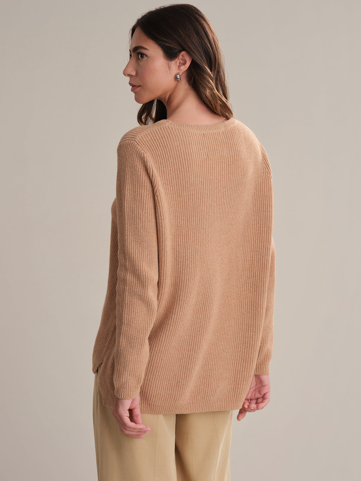 Woman wearing a beige sweater and pants against a neutral background