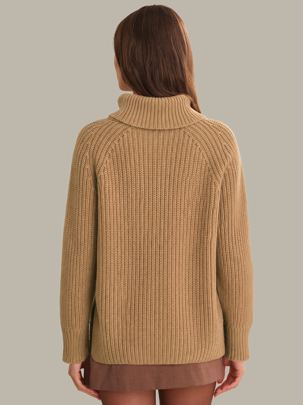 Person wearing a beige knitted sweater on a plain background