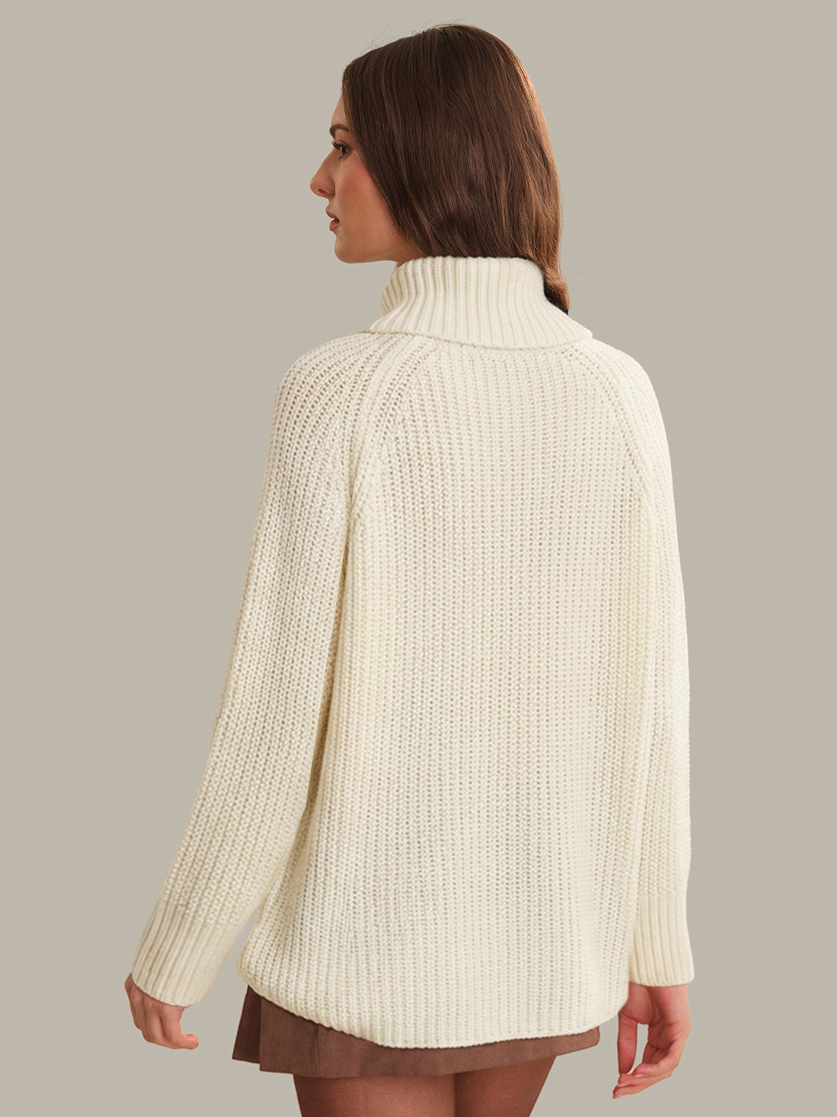 Woman wearing a cream knitted sweater against a plain background
