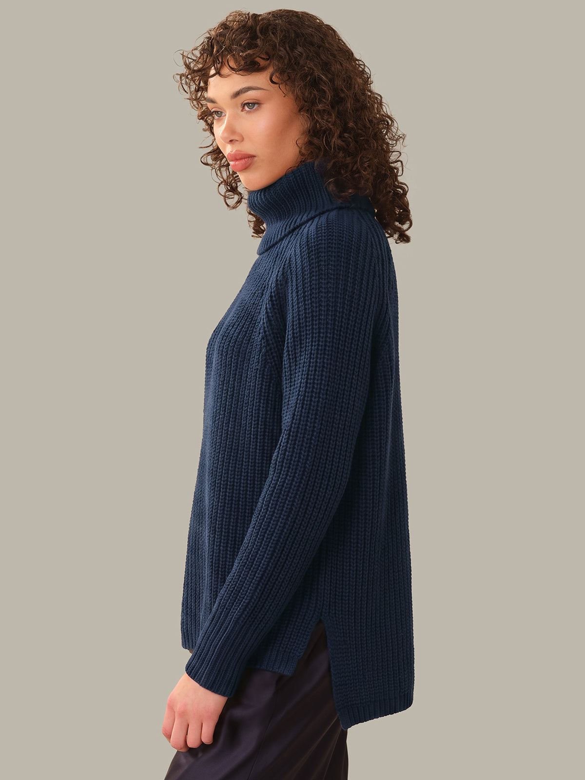 Woman wearing a navy blue ribbed turtleneck sweater against a neutral background