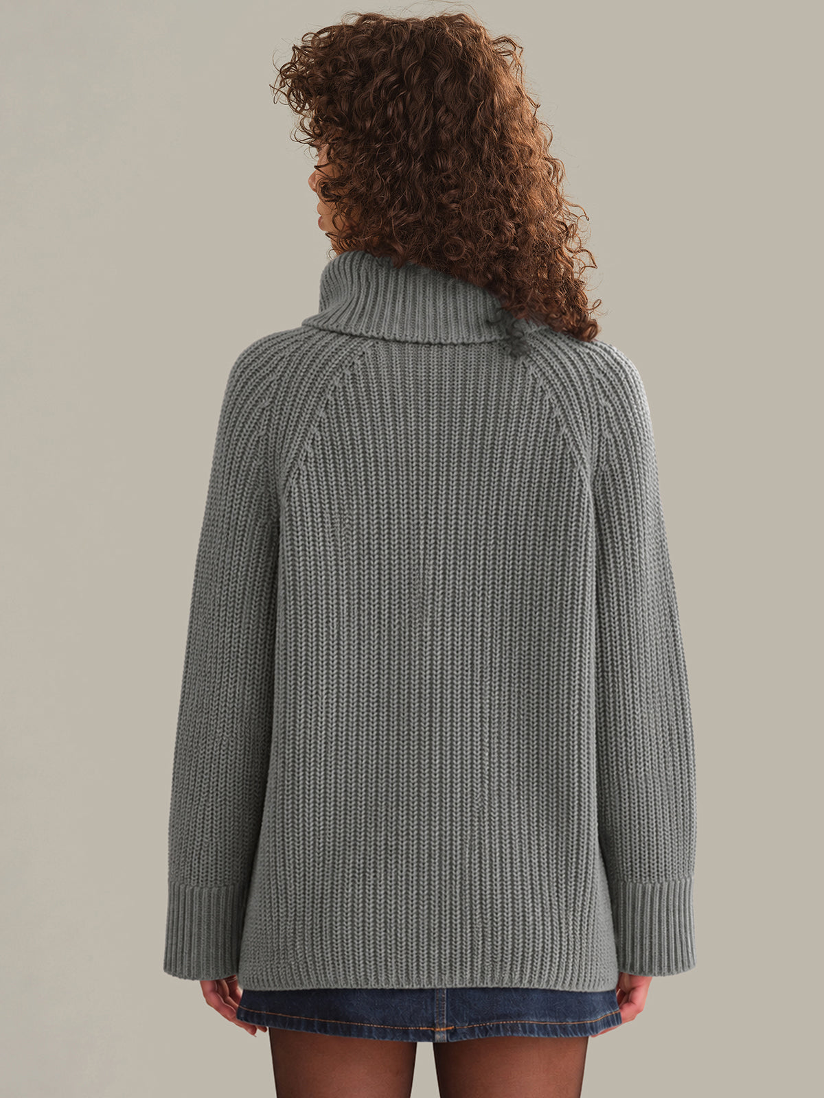 Person wearing a gray knitted sweater against a plain background