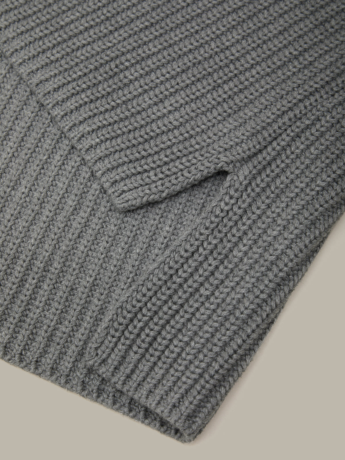 Close-up of a gray knitted sweater with a pocket on a beige background
