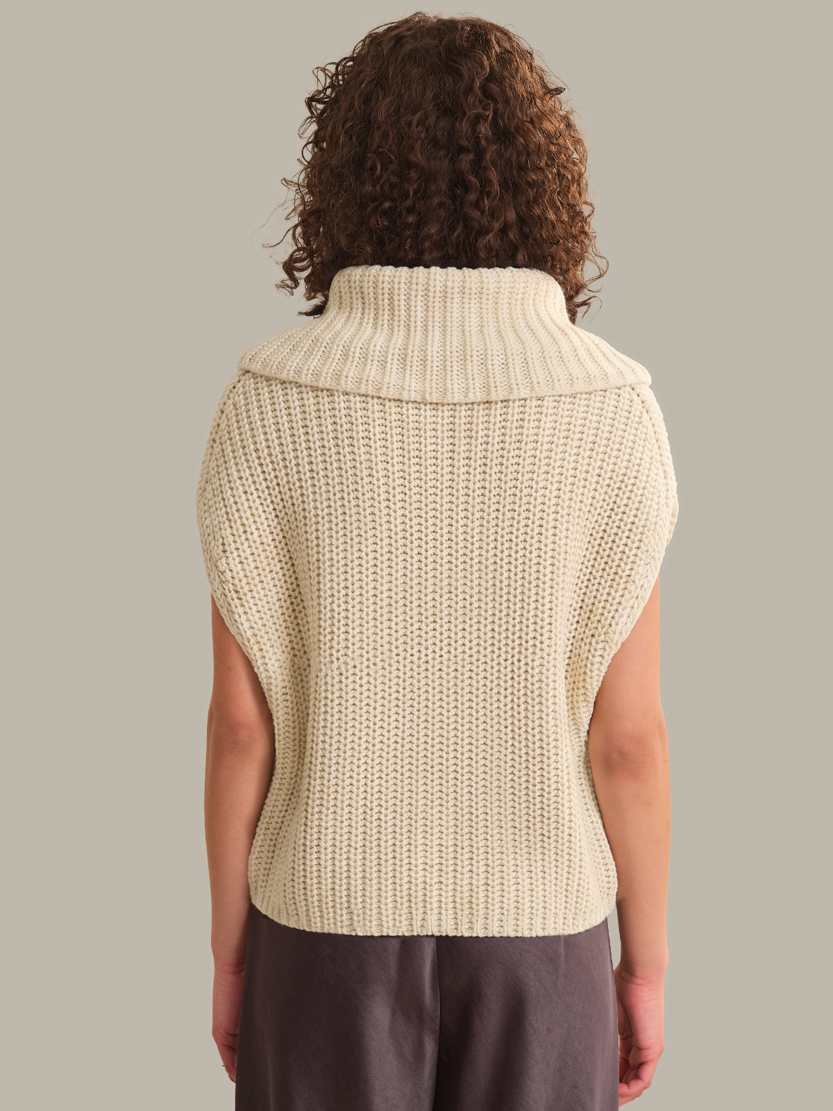 Person wearing a beige knitted vest against a neutral background